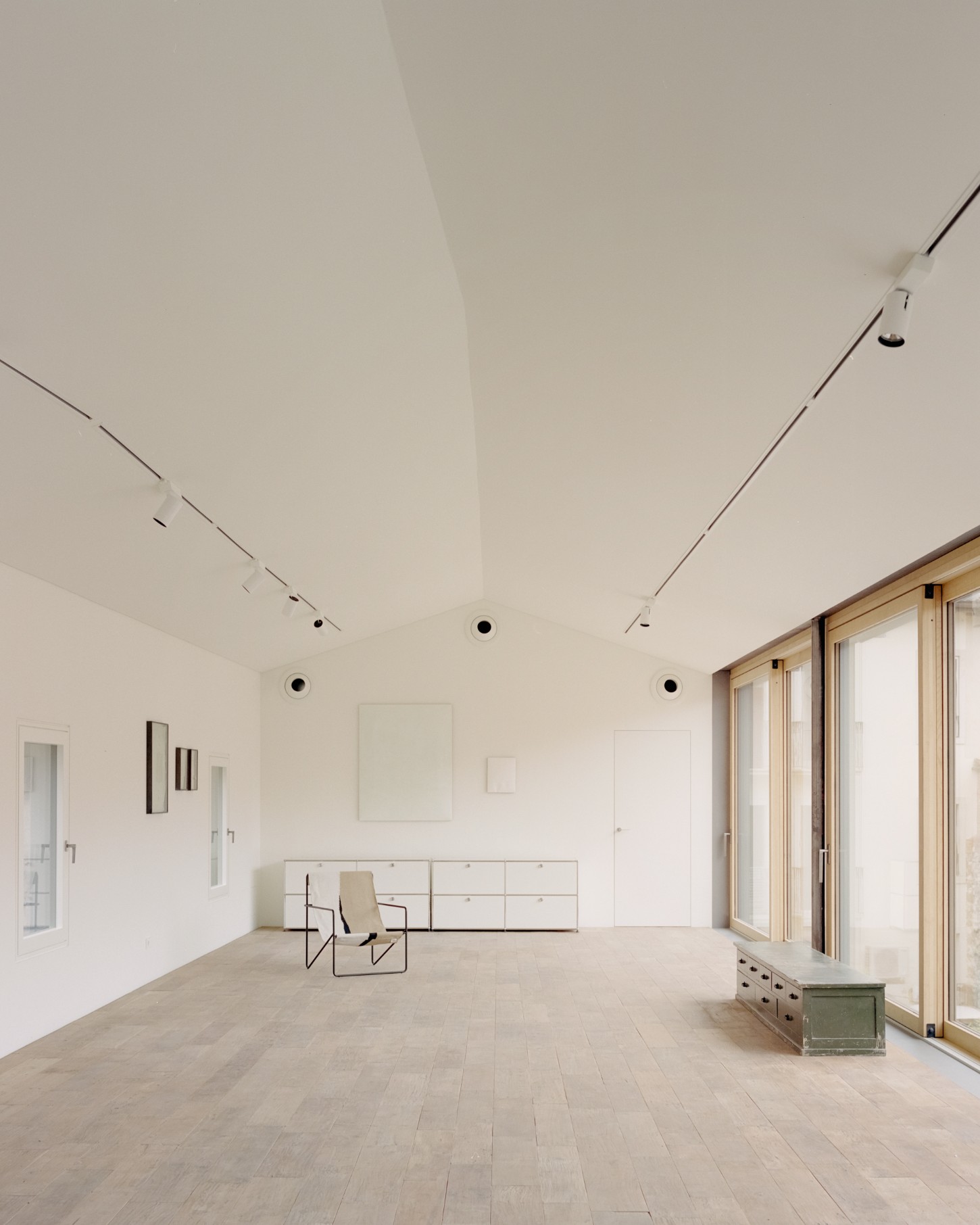 Atipografia Threshold and Treasure Gallery by AMAA — A expansive interior gallery space defined by a monolithic white ceiling with recessed track lighting and circular speaker outlets.