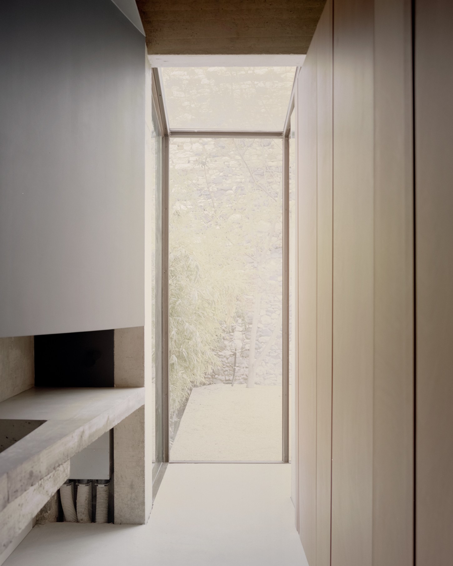 Atipografia Threshold and Treasure Gallery by AMAA — A narrow passage framed by white rendered walls and a cantilevered concrete soffit, leading toward a recessed courtyard.