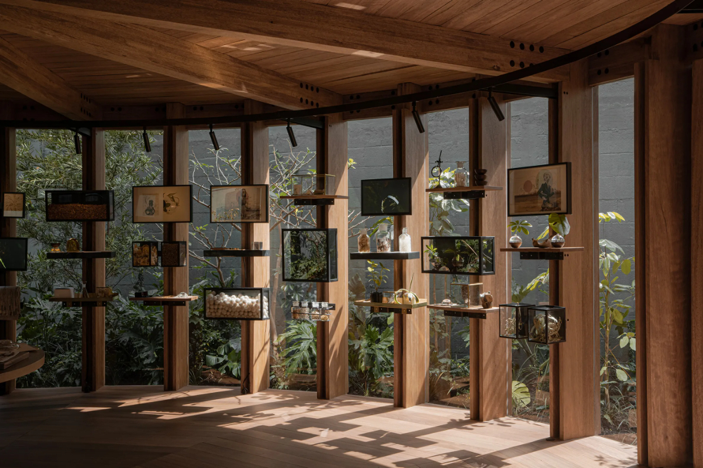 Xinú Marsella by Esrawe Studio by Estrawe Studio — A timber pavilion with radial shelving displays ceramic vessels, glass bottles, and sculptural objects at varying heights across cantilevered wooden arms.