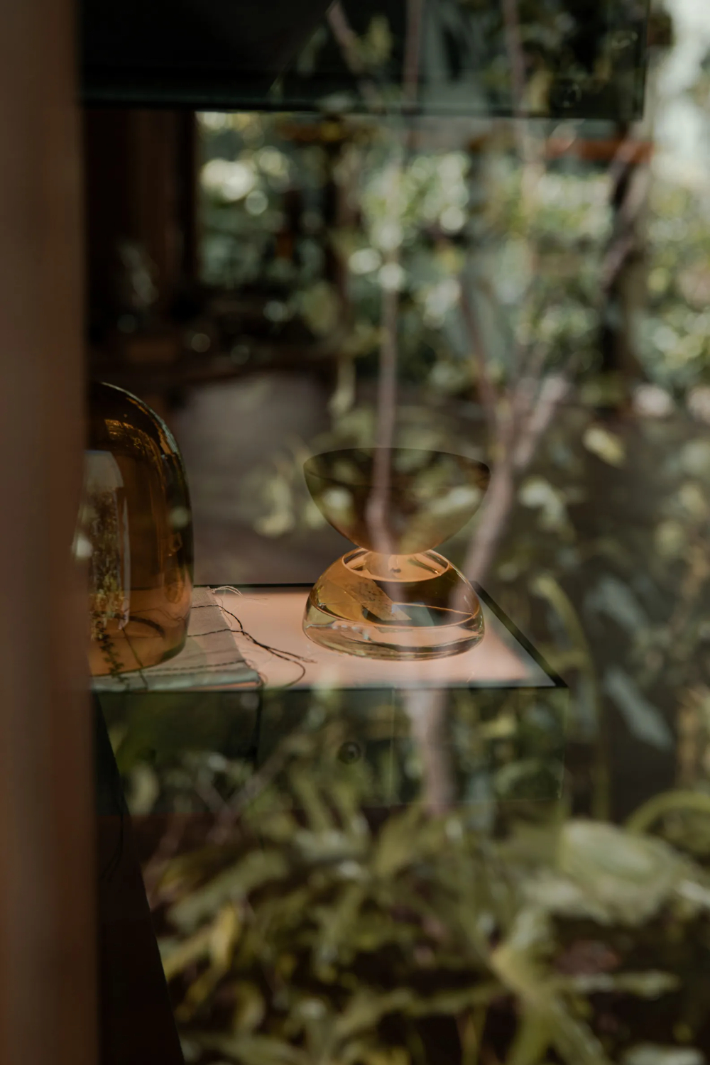 Xinú Marsella by Esrawe Studio by Estrawe Studio — A close-up detail of sculptural glass vessels displayed on a cantilevered timber shelf within the pavilion.