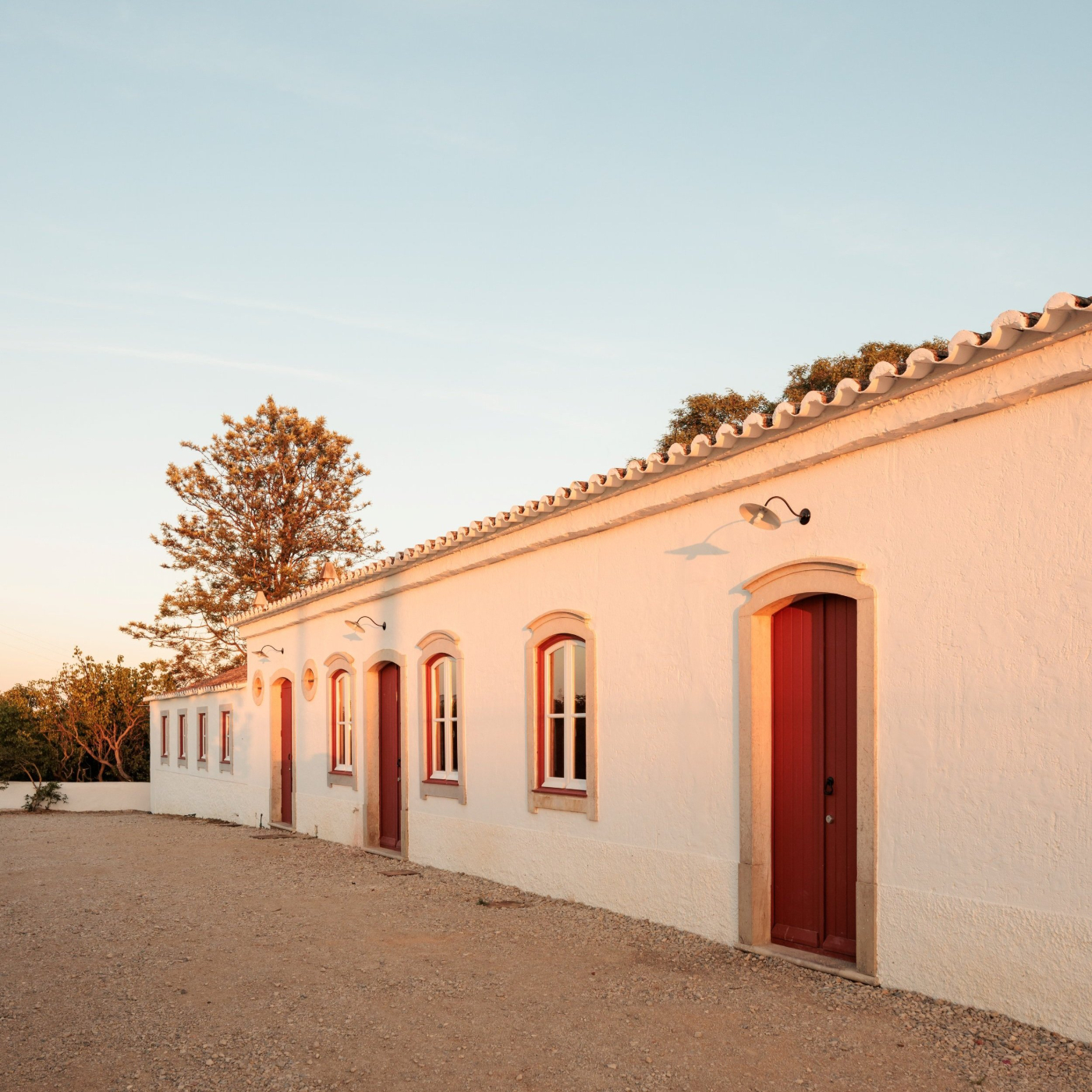 Quinta do Pinheiro by Frederico Valsassina — The whitewashed rendered facade of Quinta do Pinheiro stretches horizontally across the frame, punctuated by a series of arched window and door openings...