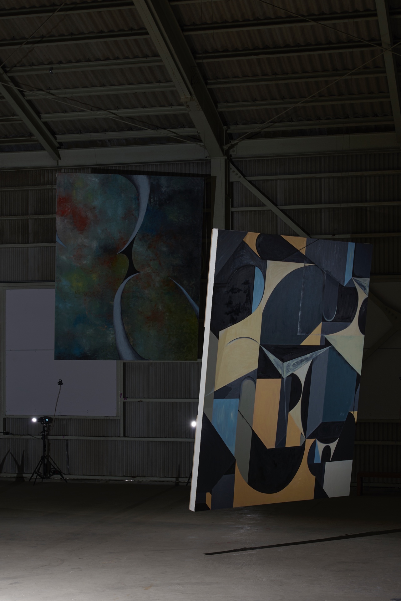 Like seeing this world for the first time by Kenji Sakai — Two large-scale artworks occupy the industrial warehouse interior: a vertical canvas suspended on the left displays abstract forms in deep blue, grey, and...