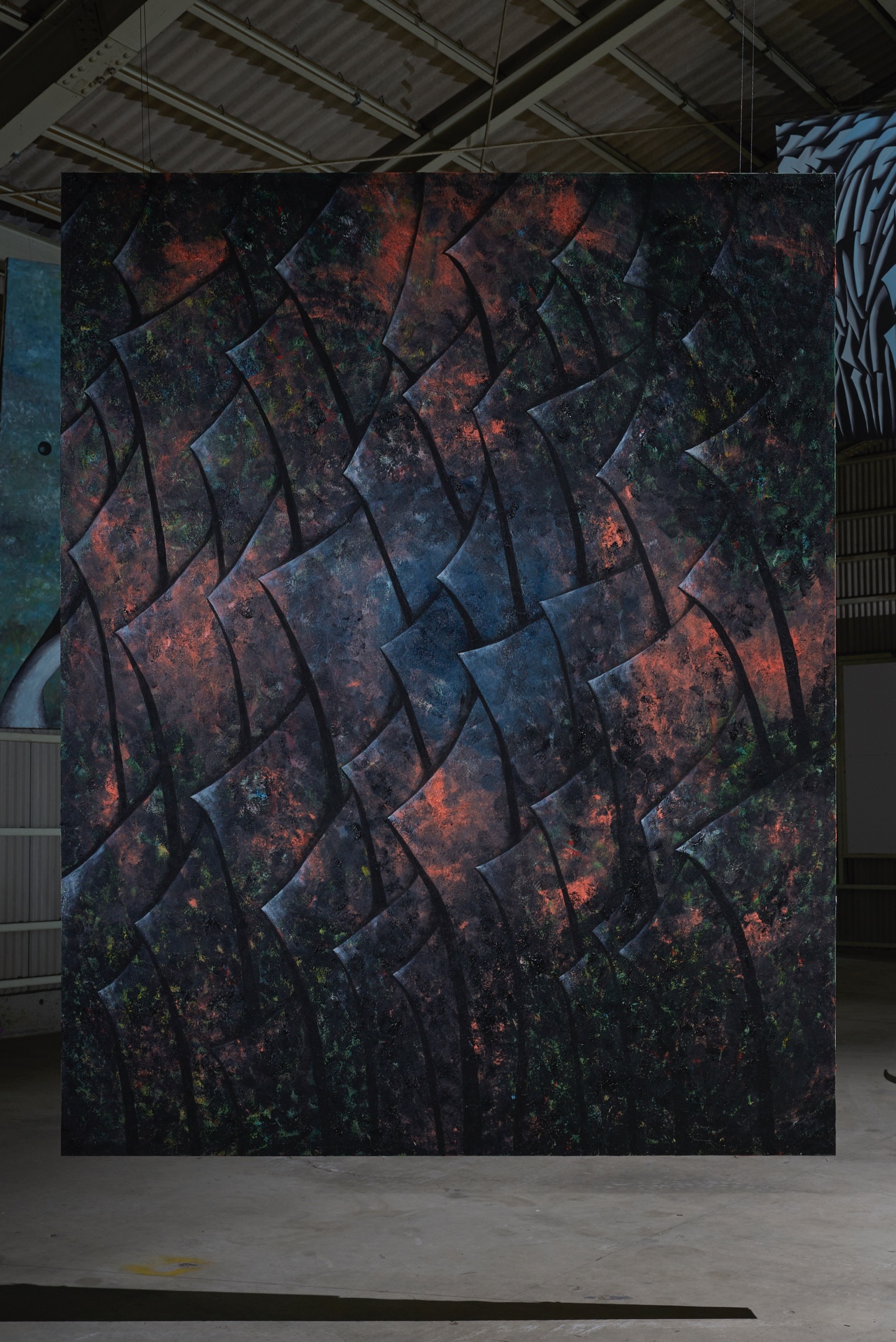 Like seeing this world for the first time by Kenji Sakai — A large-scale wall installation dominates the industrial gallery space, its surface articulated by a geometric pattern of overlapping angular panels in deep...