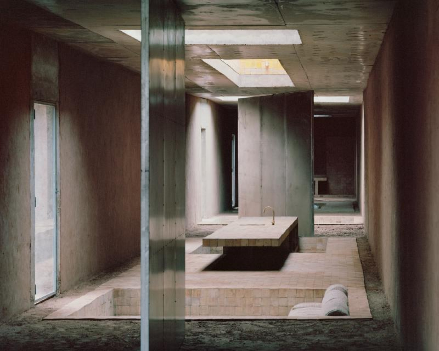 Dar El Farina by Leopold Banchini — A deep corridor perspective frames a central kitchen island with integrated sink, its recessed form anchoring the composition.