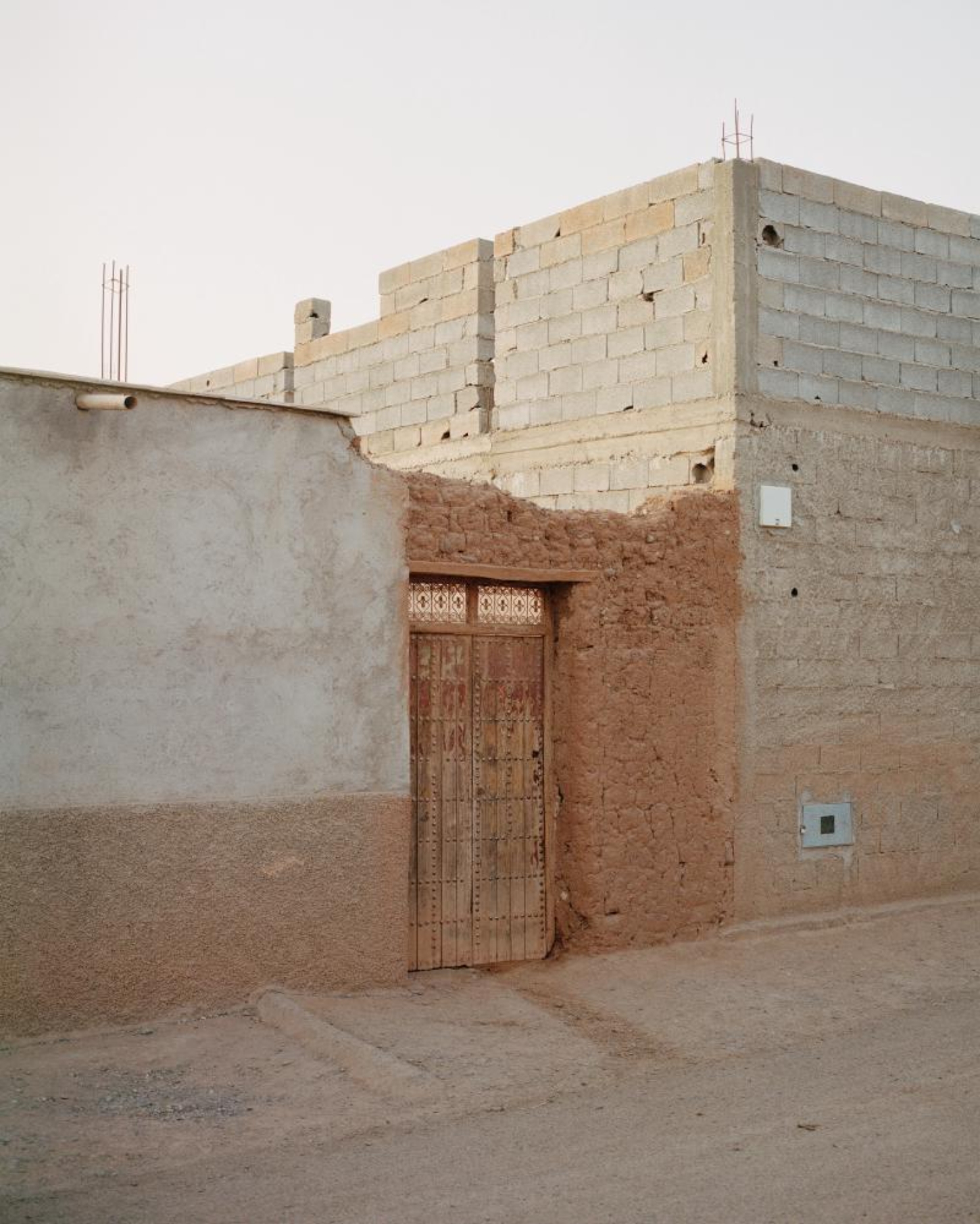 Dar El Farina by Leopold Banchini — A rammed-earth entrance facade frames a weathered timber doorway set within rendered plaster walls.