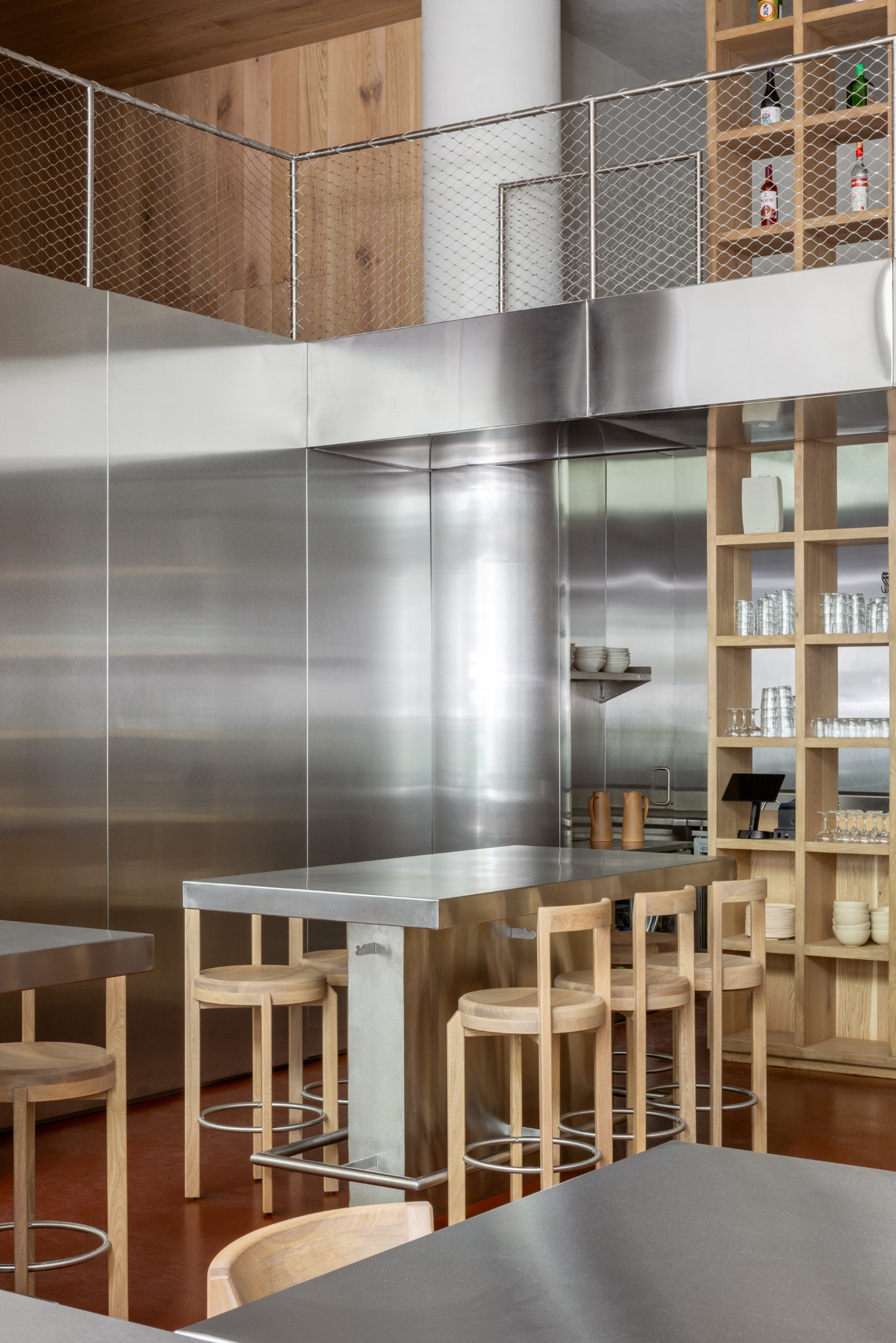 NINYAS by Ignacio Urquiza + Ana Paula de Alba — The kitchen anchors this open-plan dining space with a monolithic stainless steel volume that rises to the upper level, its horizontally seamed panels...