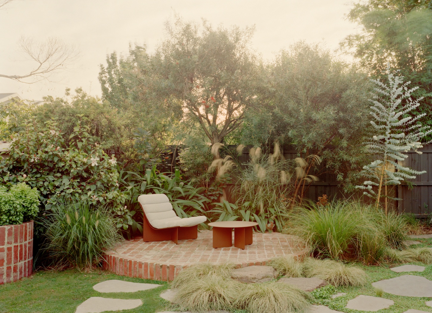 Garden Wall House by Sonelo Architects — A garden courtyard anchors the rear outdoor space, defined by a circular brick paving pattern edged in terracotta.