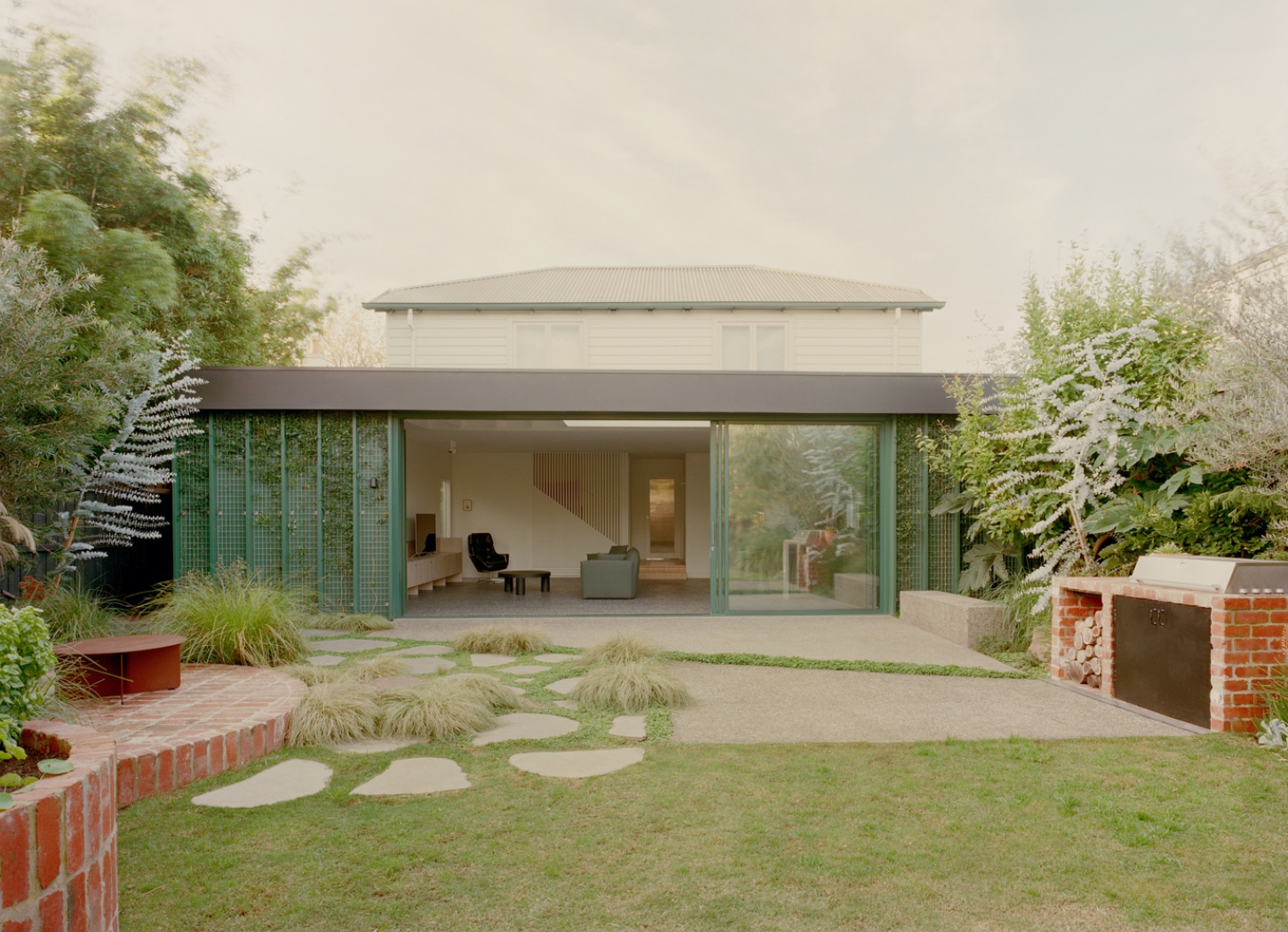 Garden Wall House by Sonelo Architects — The Garden Wall House's south-facing elevation opens to the landscape through deep forest-green aluminum framing with vertical grid patterning.