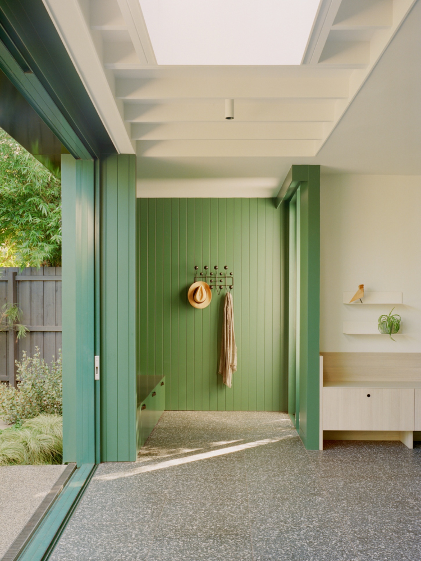 Garden Wall House by Sonelo Architects — A garden-facing corridor features deep forest-green vertical battening on the interior wall, echoing the aluminum-framed sliding doors that open to the...