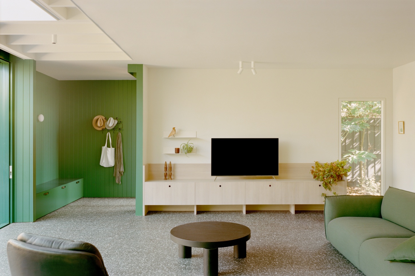 Garden Wall House by Sonelo Architects — The living room centers on a minimalist entertainment wall clad in timber with integrated shelving and a centered television.