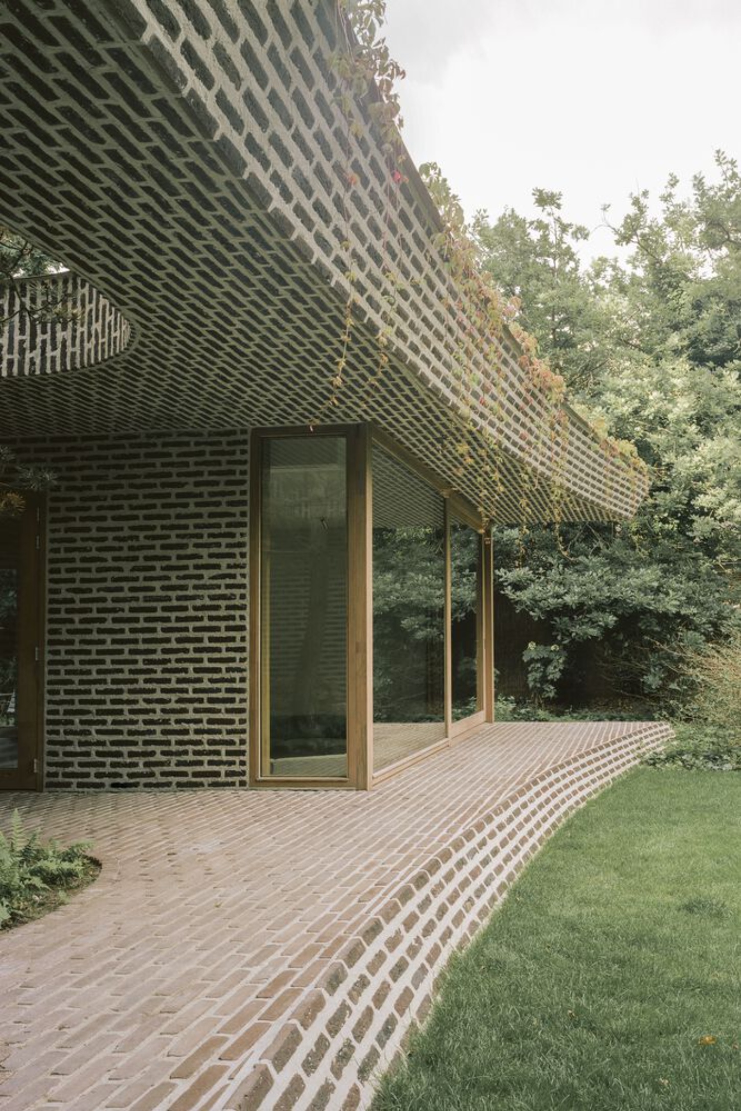 BD House by Space Encounters + Studio Vincent Architecture — The rear facade of BD House presents a studied composition of horizontal brick coursing interrupted by flush glass sliding doors spanning the full width.