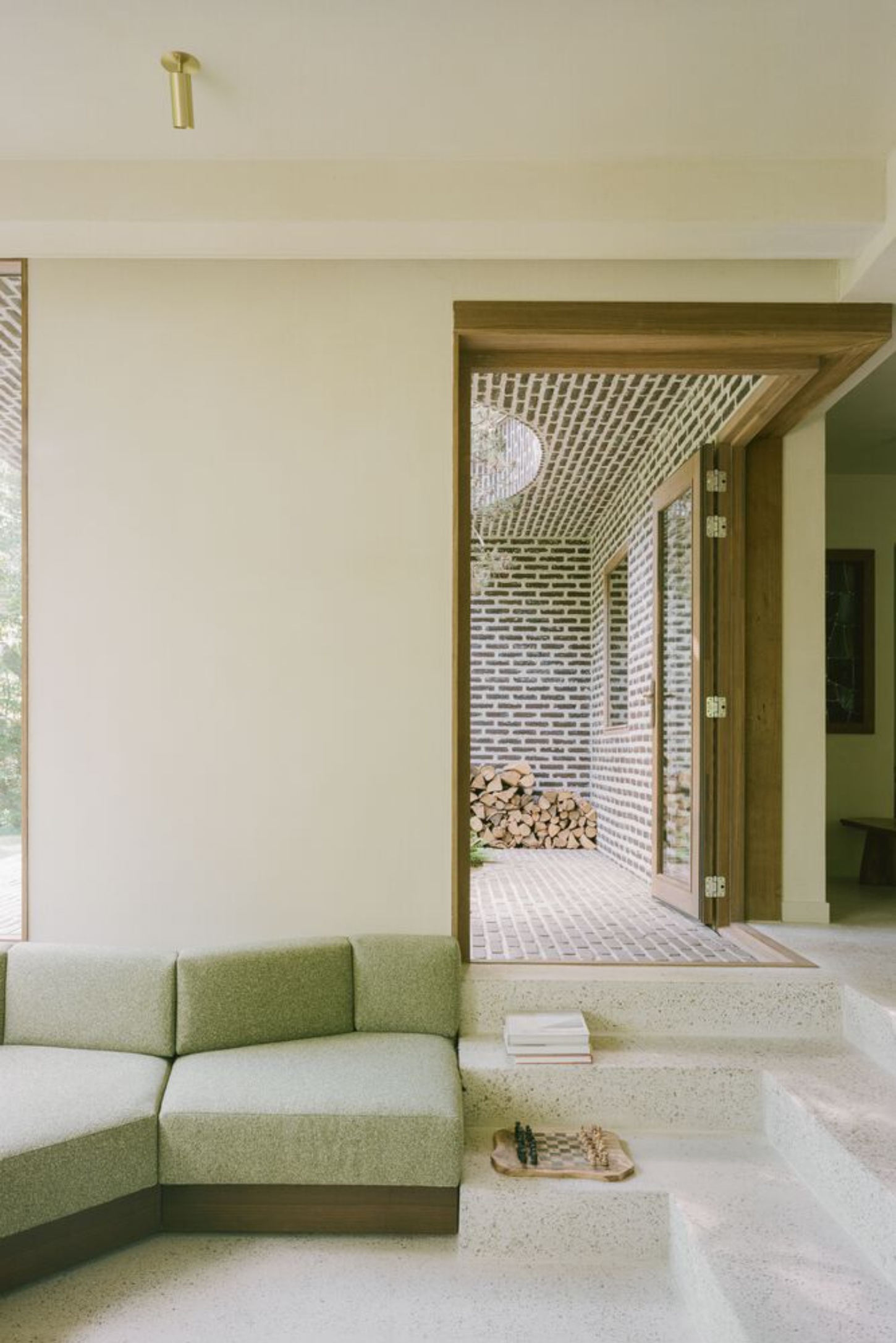 BD House by Space Encounters + Studio Vincent Architecture — A living room interior frames the threshold to an enclosed courtyard garden beyond.