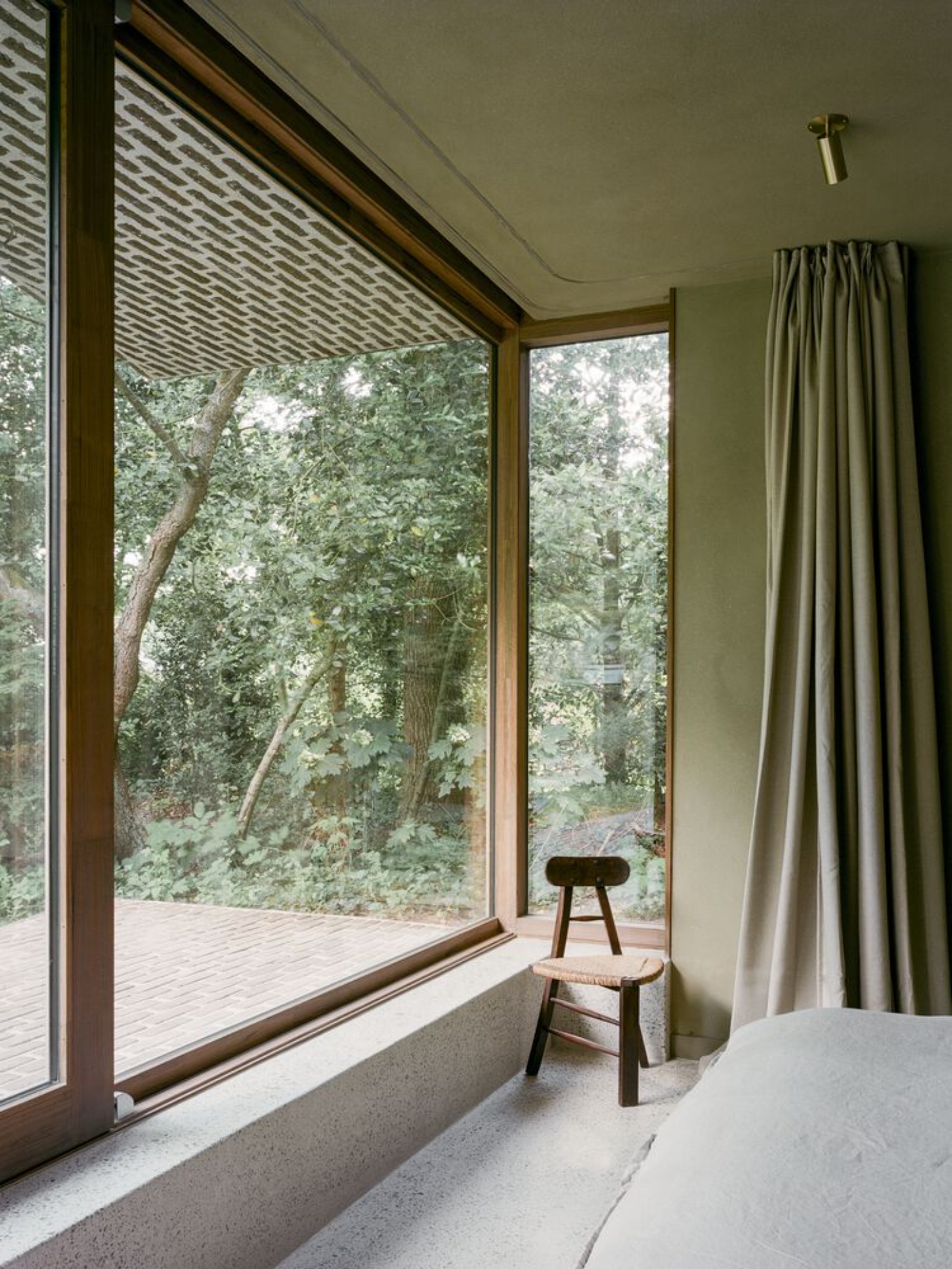 BD House by Space Encounters + Studio Vincent Architecture — A timber-framed glazed room opens fully to the forest beyond through flush glass sliding doors, the transparent threshold dissolving interior from landscape.
