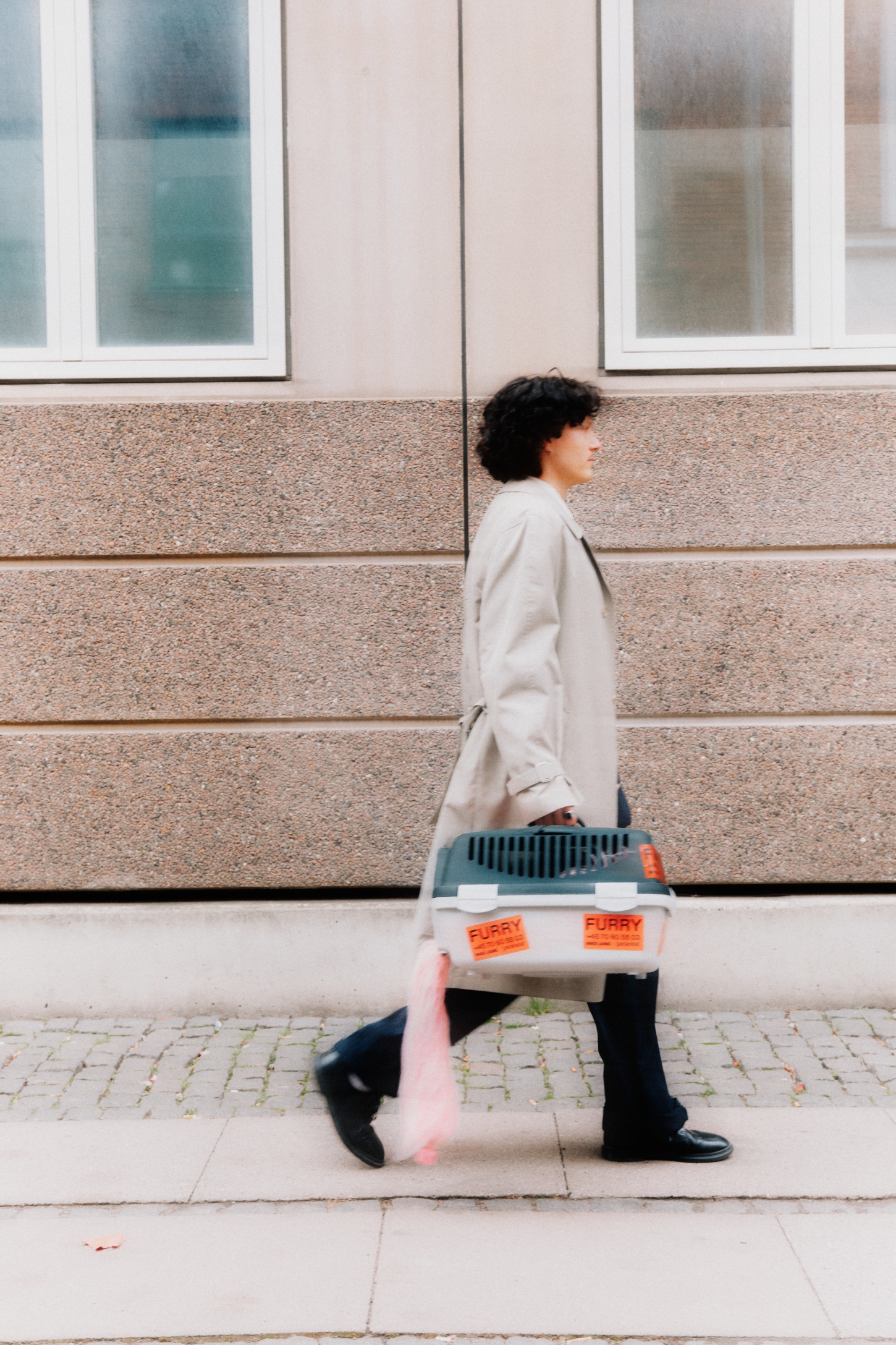 FURRY by Pedestal x NIKO JUNE — A person in a cream-colored blazer carries the FURRY cord sleeve down a Copenhagen street, its soft pink synthetic fur cascading vertically against their body.