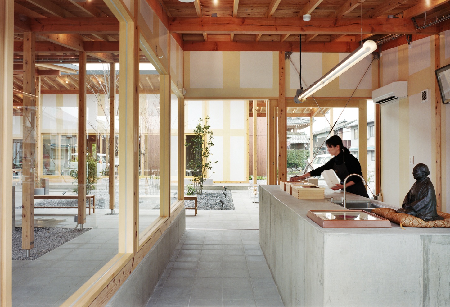 Funamachi Base Store by Jo Nagasaka + Schemata Architects — The storefront presents a linear passage defined by post-and-beam timber construction, with exposed reddish beams overhead and regular spacing visible...