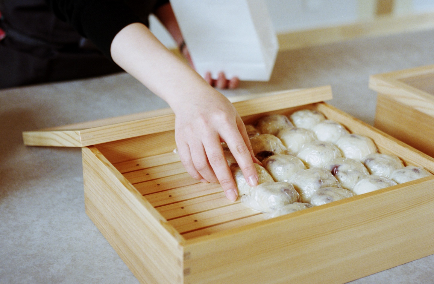 Funamachi Base Store by Jo Nagasaka + Schemata Architects — A wooden steamer basket with horizontal slat construction reveals stacked dumplings arranged in neat rows, their pleated edges and pale dough visible...