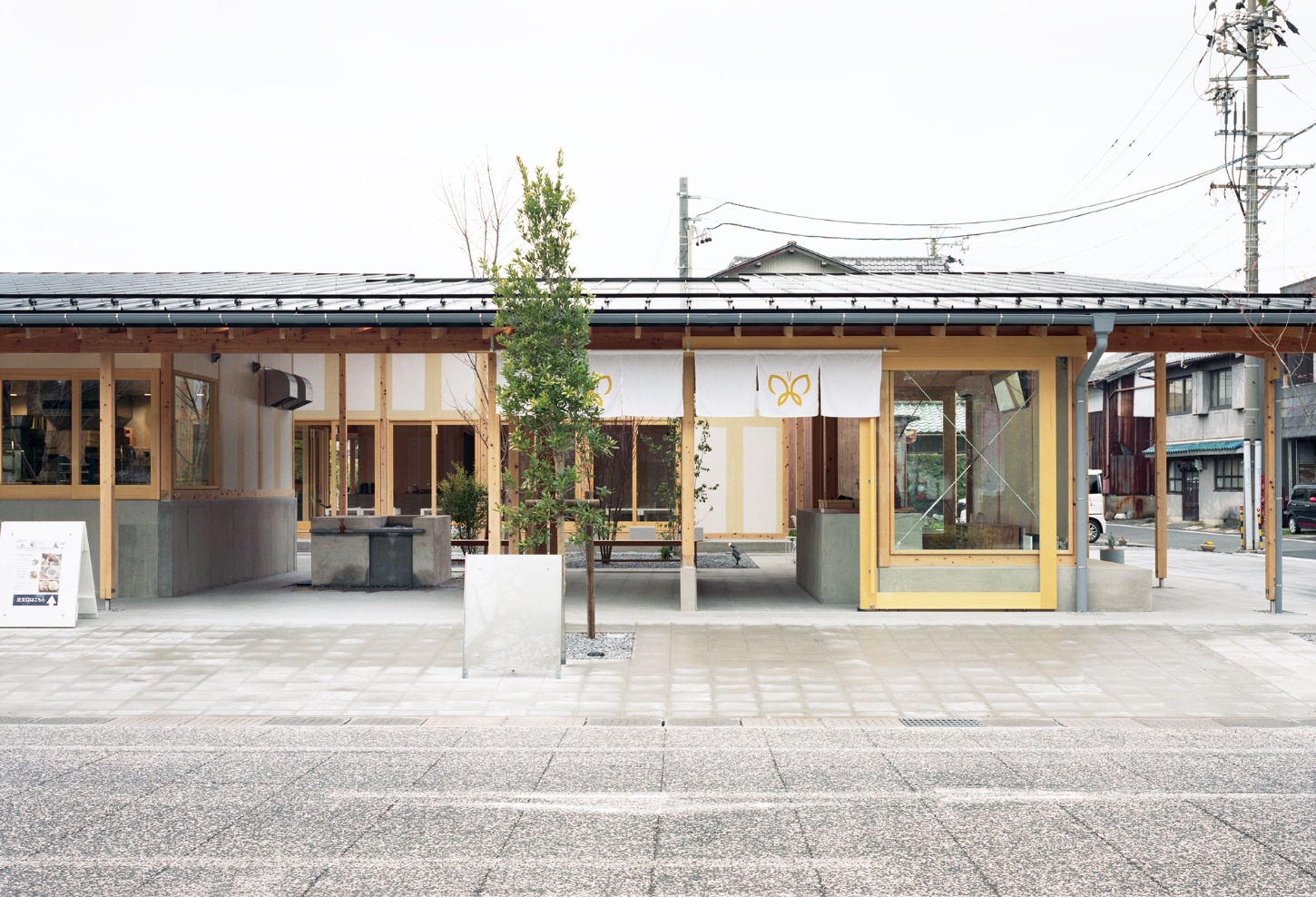 Funamachi Base Store by Jo Nagasaka + Schemata Architects — The storefront presents a post-and-beam timber frame with regular grid overhead, supporting a dark metal roof with visible fasteners.