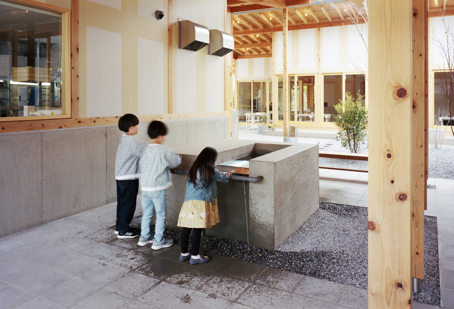 Funamachi Base Store by Jo Nagasaka + Schemata Architects — Three children interact with a monolithic concrete counter positioned within the open-plan ground floor.