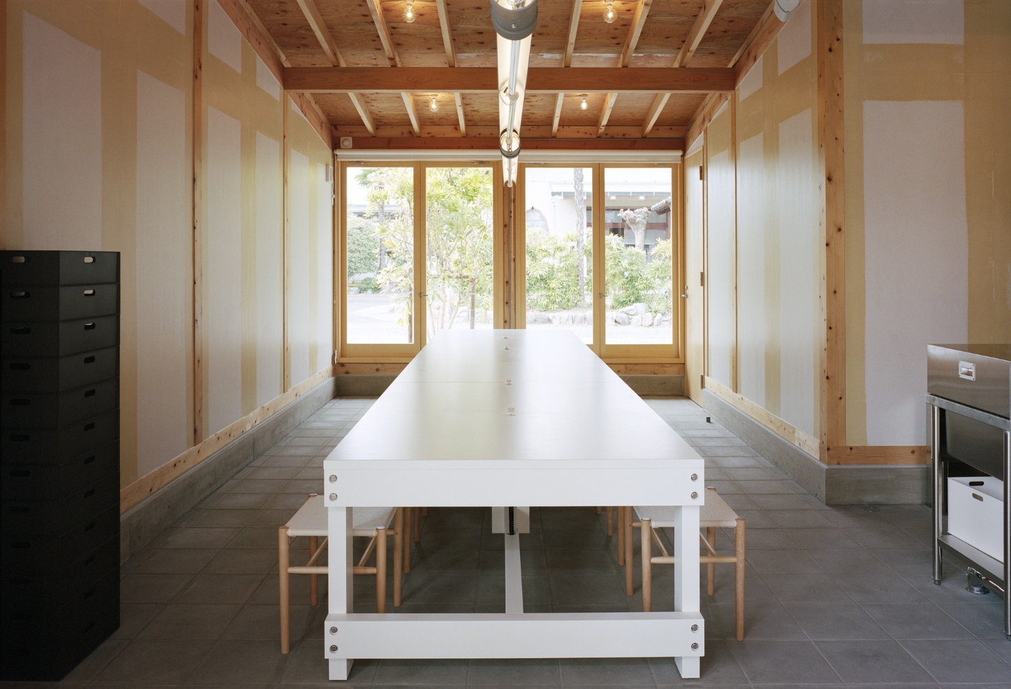 Funamachi Base Store by Jo Nagasaka + Schemata Architects — A longitudinal view of the communal dining space reveals the post-and-beam structural logic: exposed timber beams grid the ceiling at regular intervals with...