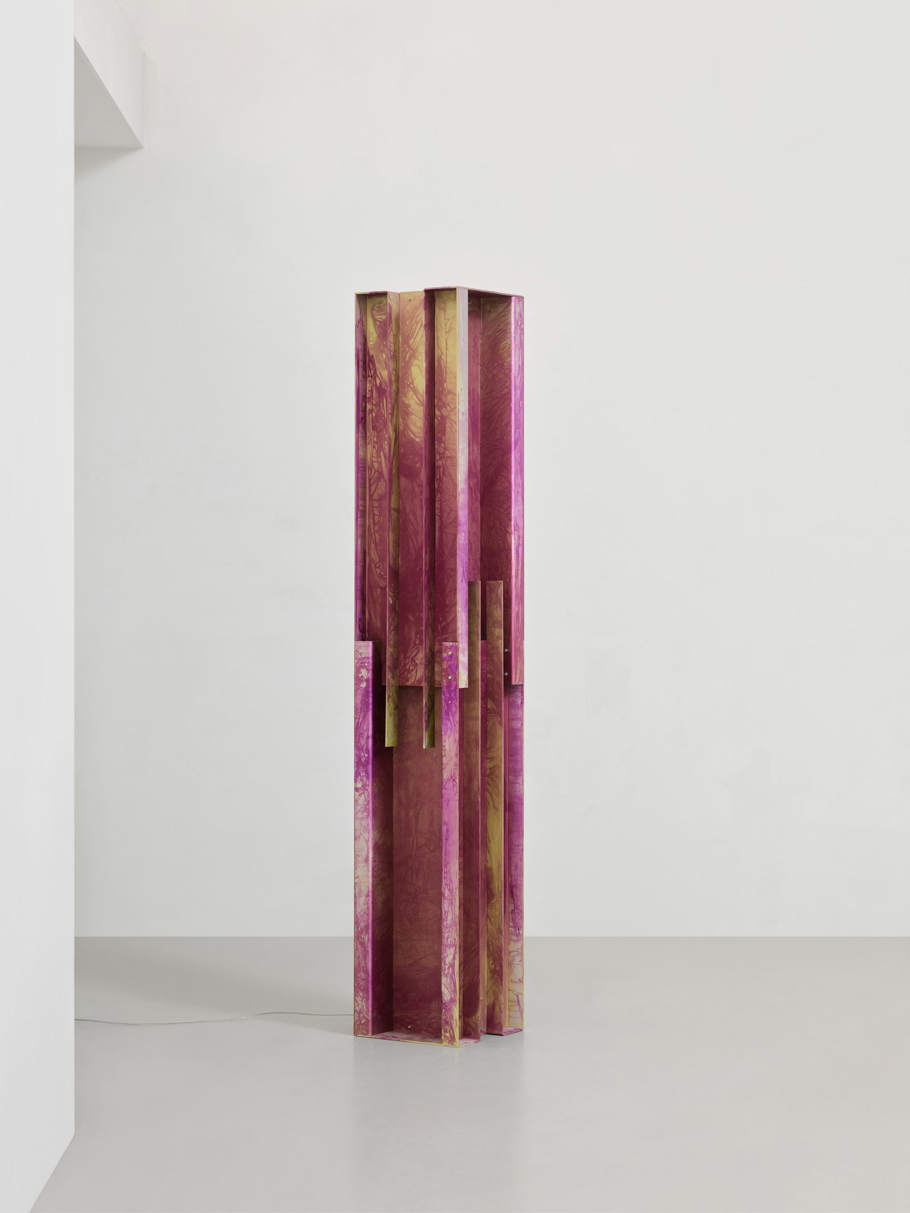 Anodized Collection by Paul Coenen — A tall, slender anodized aluminum column dominates the white gallery space, its surface characterized by rippling patterns in deep violet with ochre and...
