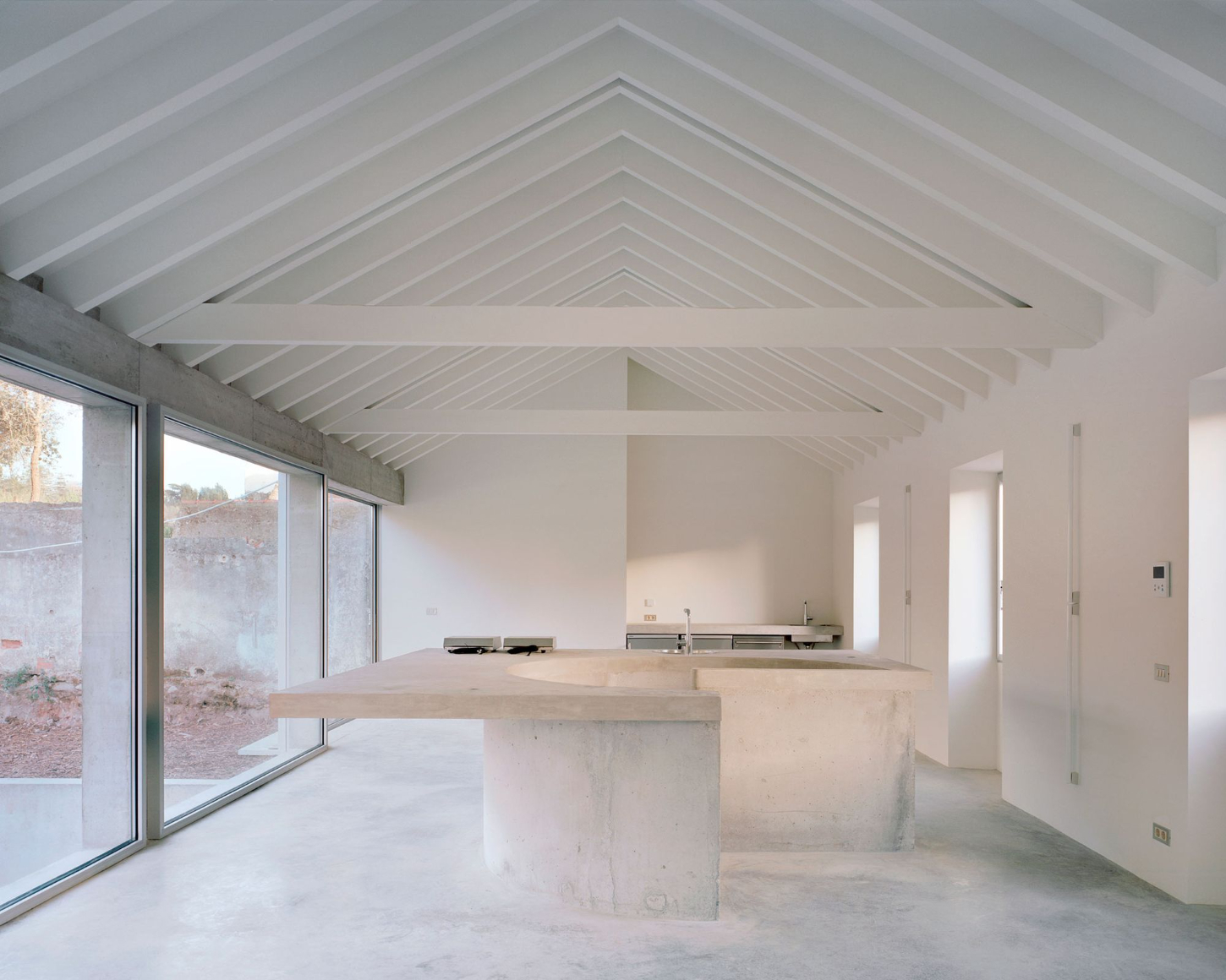 Tenant House by Arquitectura-G — A monolithic concrete kitchen island anchors the open-plan interior, its sculptural form housing a circular integrated sink and steel tap.