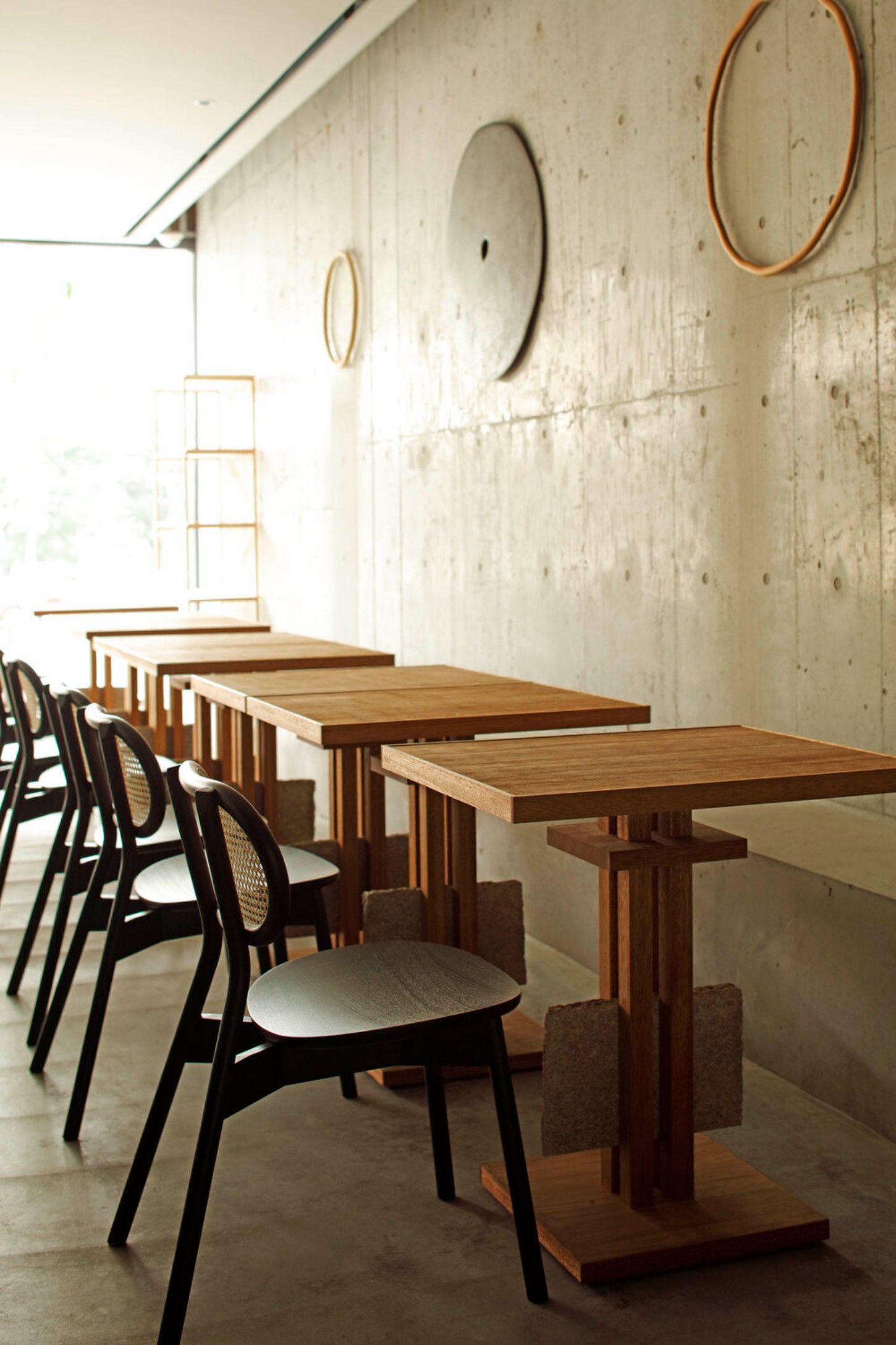 OGAWA COFFEE LABORATORY by Yusuke Seki Studio — Three timber tables with warm grain detail are arranged in linear succession, each paired with black-framed chairs featuring woven cane backrests and...