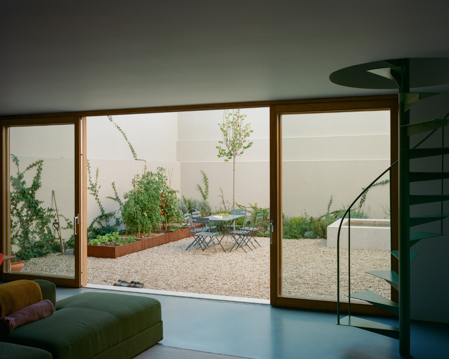 Marvilla House by Atelier José Andrade Rocha — Interior view through timber-framed sliding glass doors onto a gravel courtyard garden.