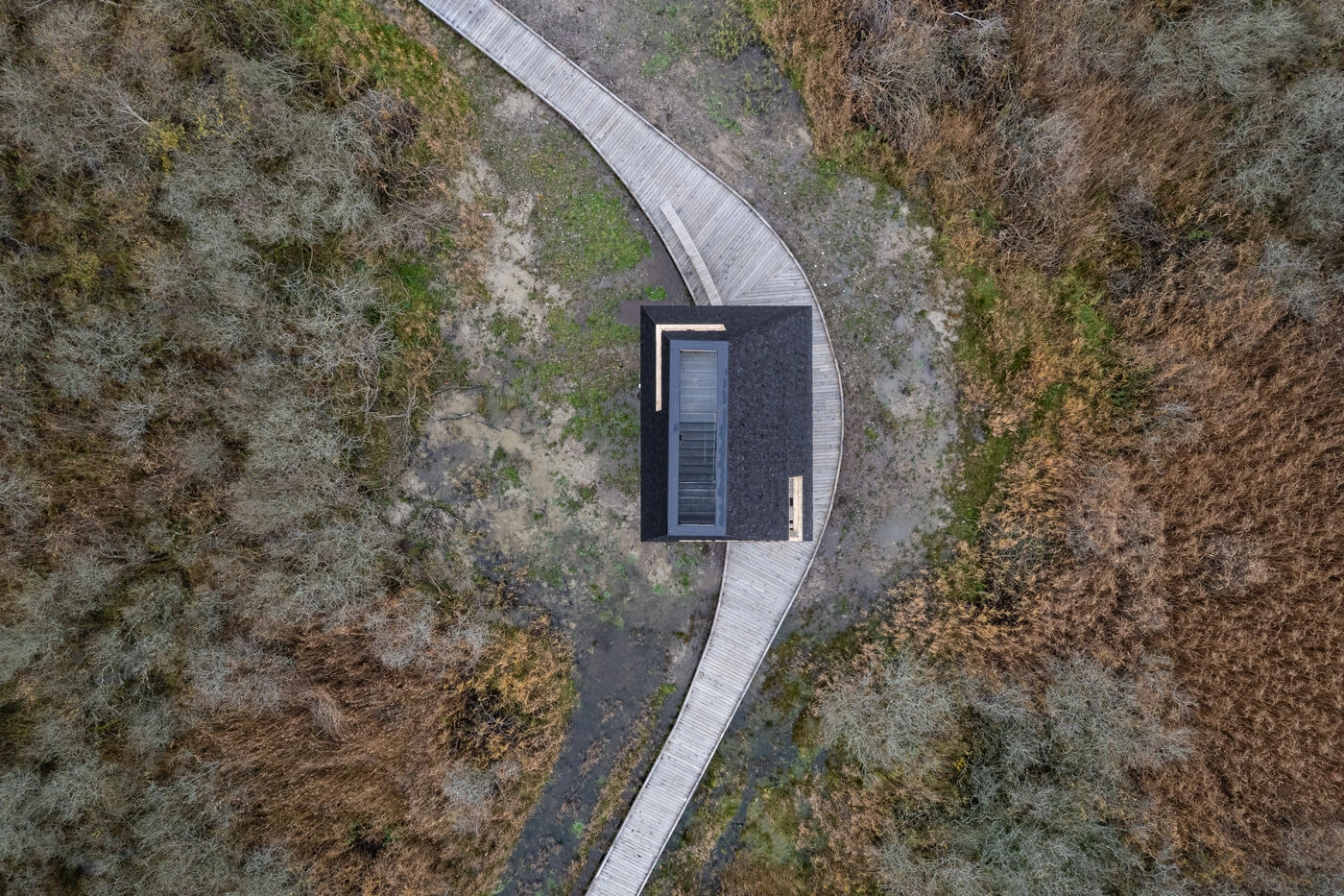 Amager Nature Park by ADEPT and LYTT Architecture — Aerial view of a visitor pavilion at Amager Nature Park, its dark cedar-shingle exterior forming a geometric volume with a conical roof.