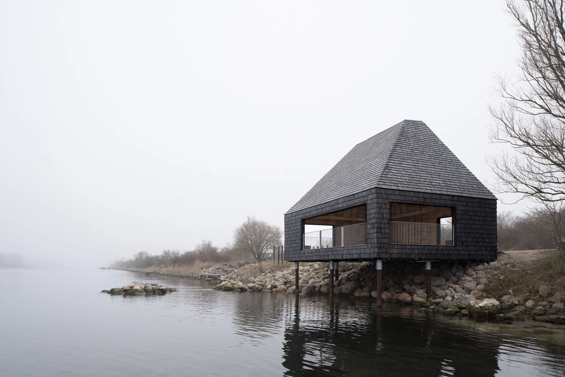Amager Nature Park by ADEPT and LYTT Architecture — A single-story visitor pavilion on the Amager Nature Park perimeter, elevated on wooden pilings above the water's edge.