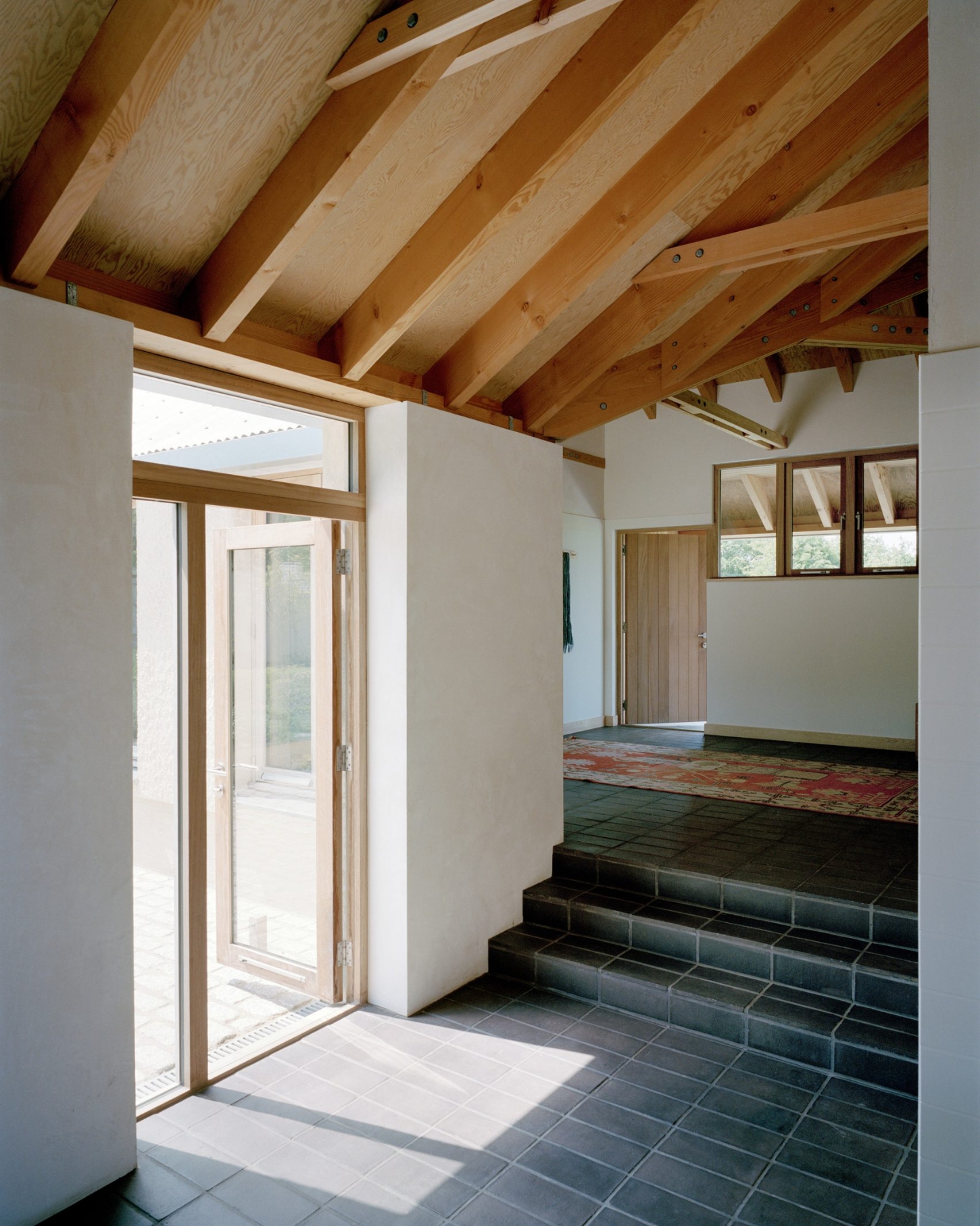 Farmworker's House by Hugh Strange Architects — Interior view of the entrance hall featuring exposed timber roof beams with visible fasteners and a clerestory window strip.