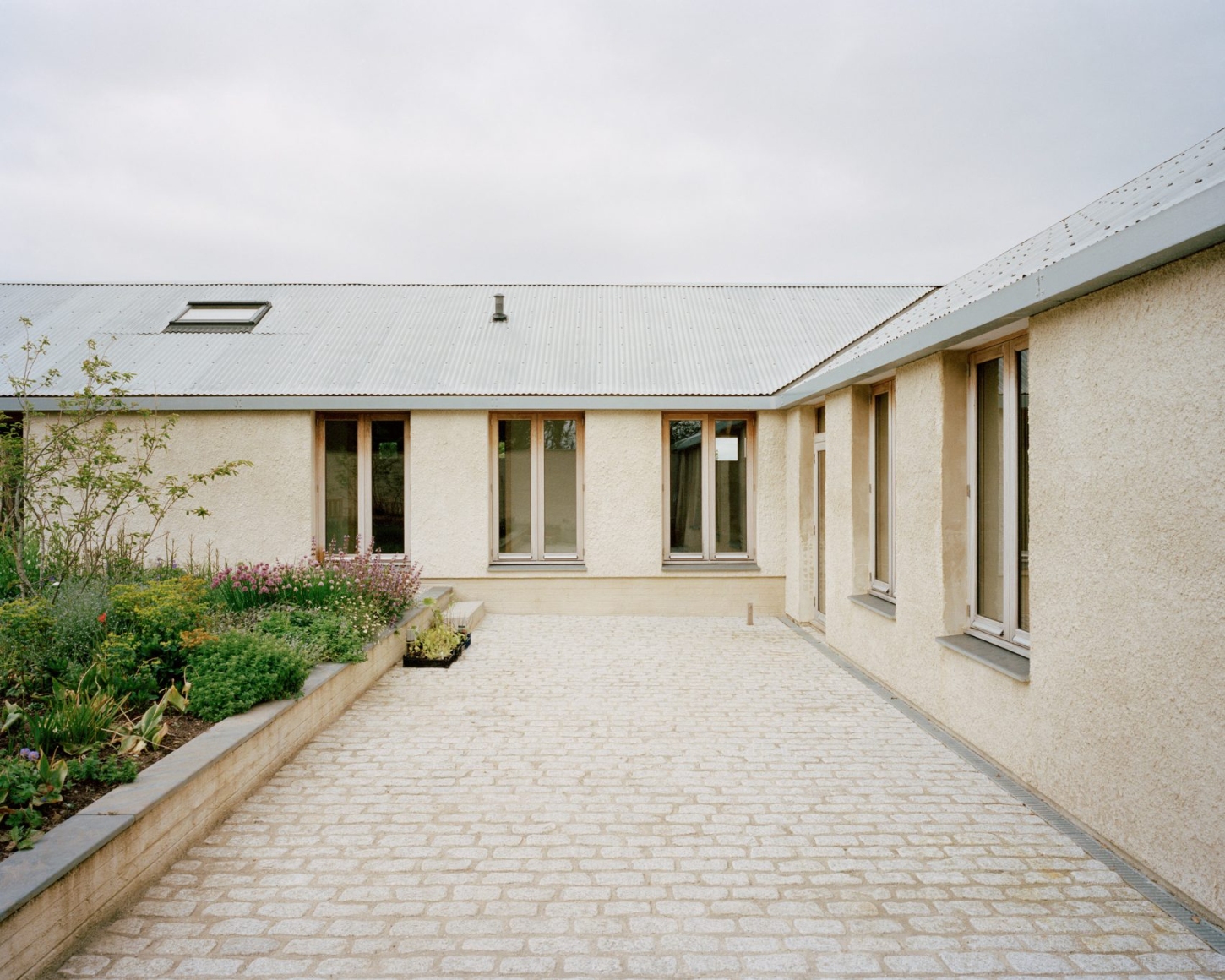 Farmworker's House by Hugh Strange Architects — A cream-rendered courtyard elevation of the Farmworker's House reveals the protective L-shaped plan characteristic of agricultural compounds.