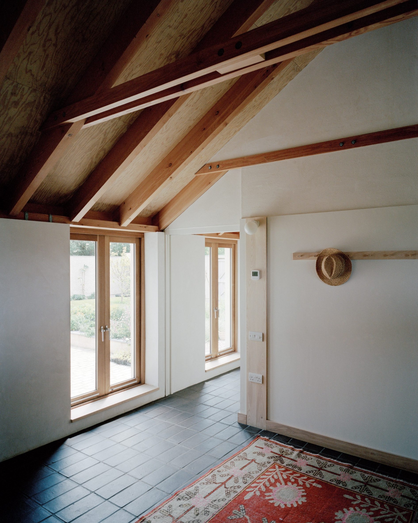Farmworker's House by Hugh Strange Architects — An interior passage framed by exposed timber roof trusses in alternating oak and lighter wood, their geometry cast in sharp relief against white gypsum board.