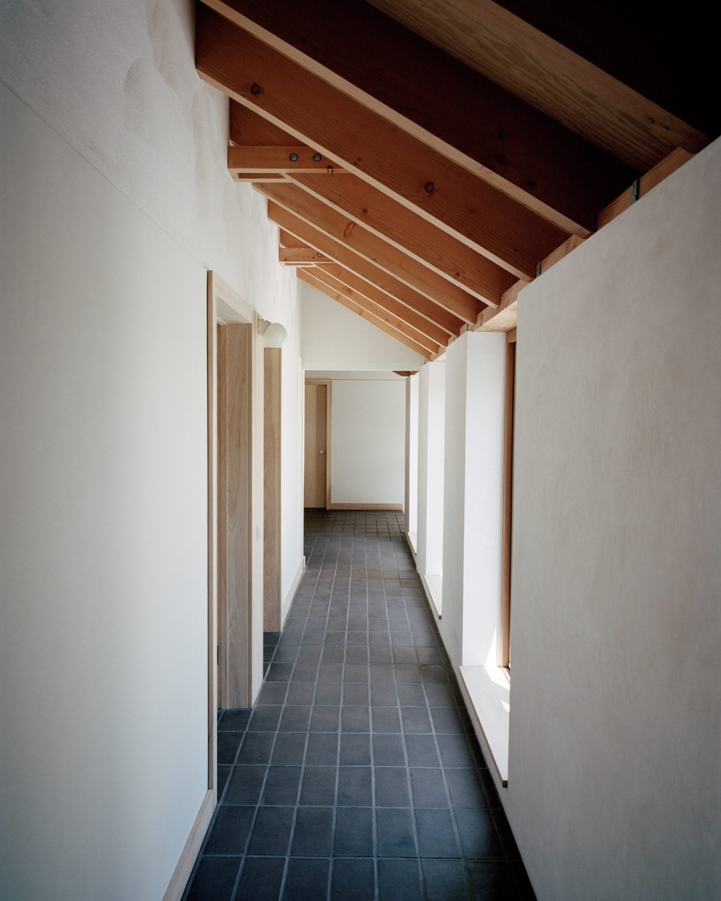 Farmworker's House by Hugh Strange Architects — A linear corridor extends through the farmworker's house, its dark slate-tiled floor contrasting sharply with cream-rendered walls.