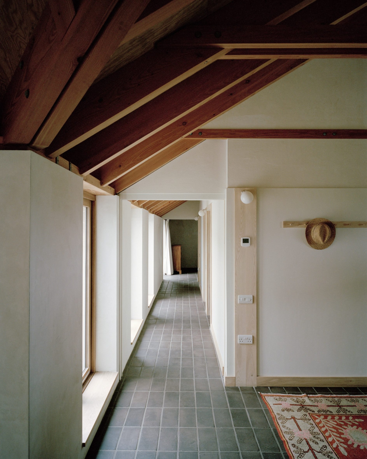 Farmworker's House by Hugh Strange Architects — A long hallway extends through the interior of the farmworker's house, framed by white-rendered walls and punctuated by timber door frames in natural wood...