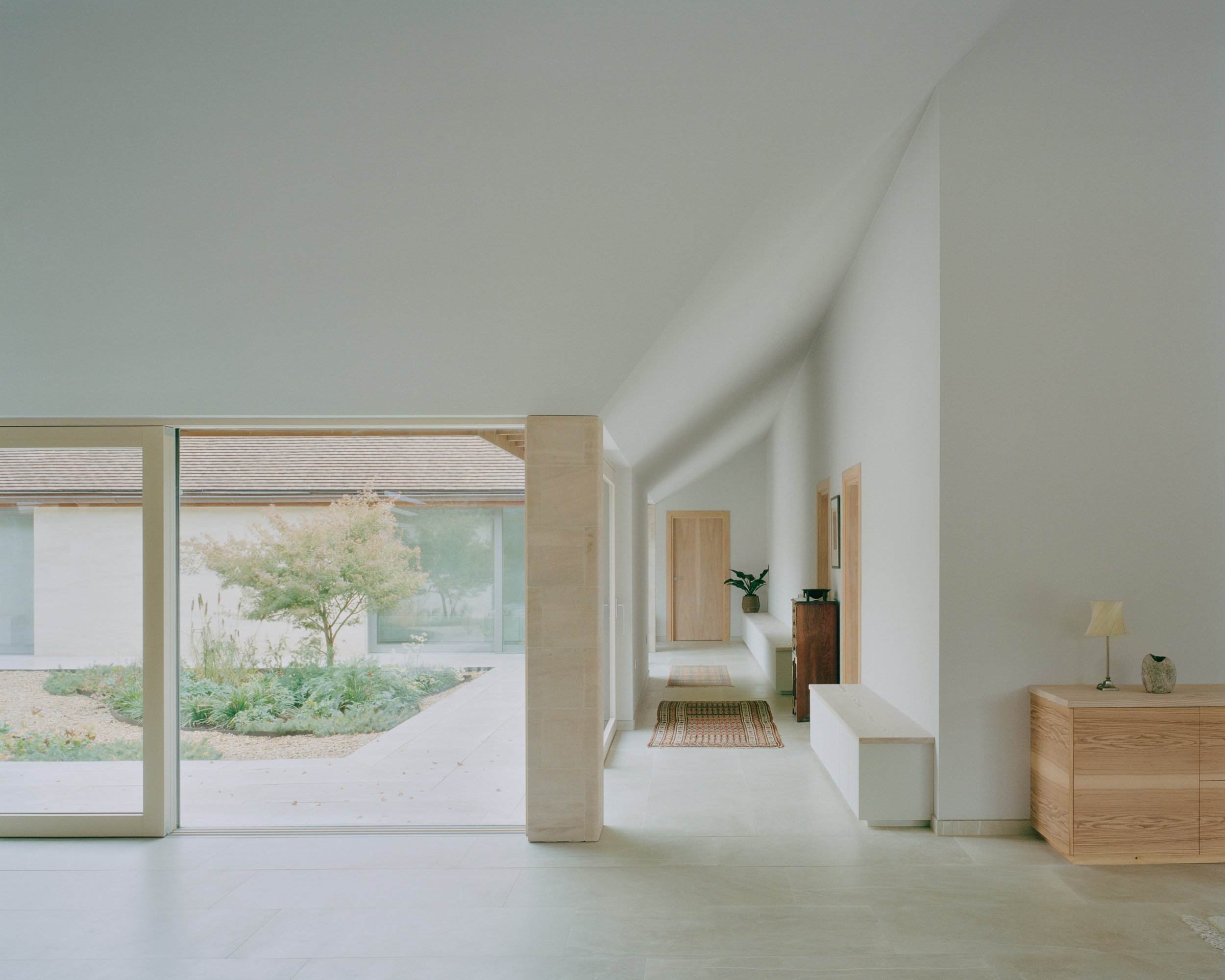 Eavesdrop by Tom Dowdall — Interior passage flooded with directional daylight from a southwest-facing pitched roof, articulating the Passivhaus thermal envelope.
