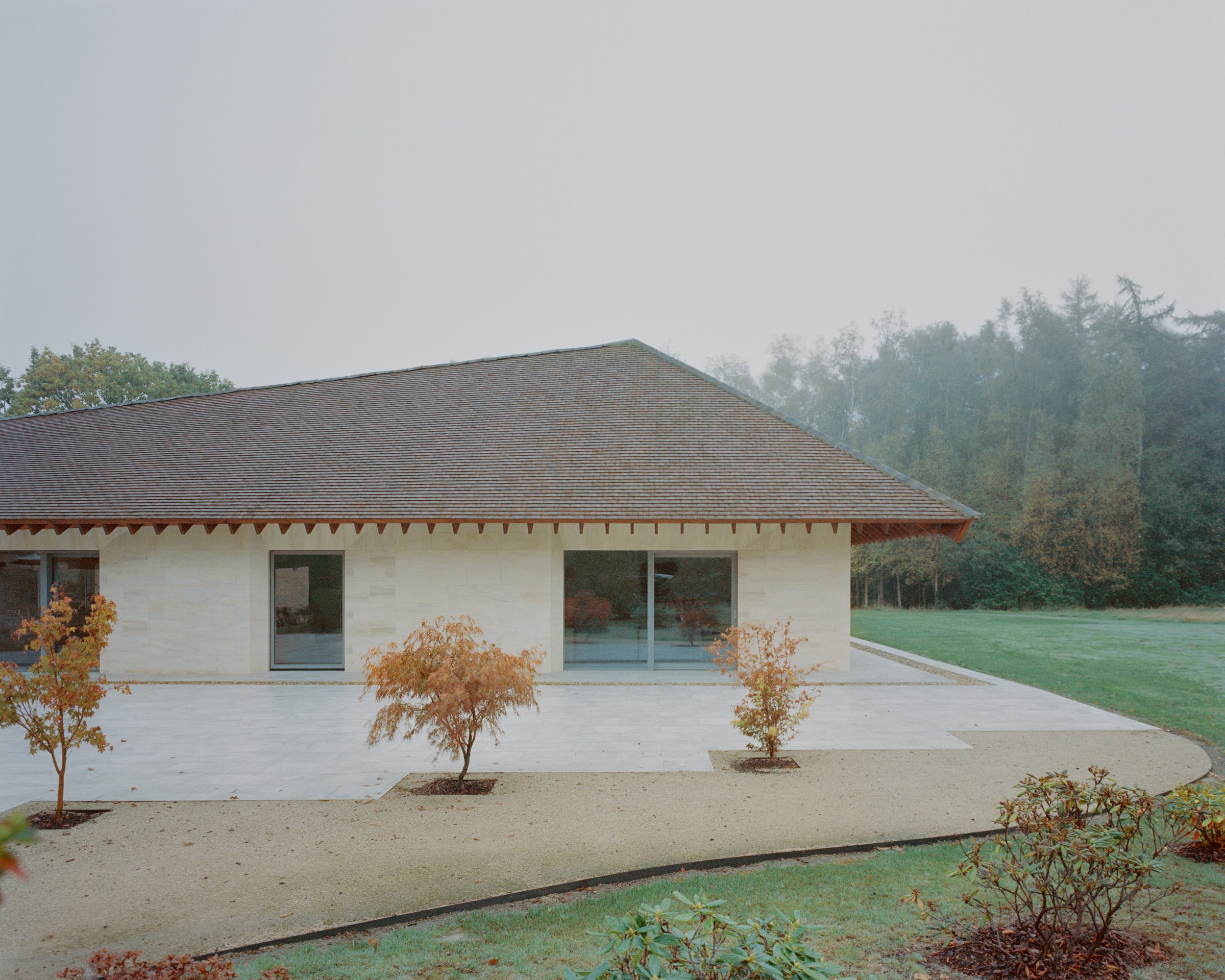 Eavesdrop by Tom Dowdall — The rendered facade of Eavesdrop presents a continuous horizontal glazing band across white walls, articulated by timber soffit detailing at the eaves.