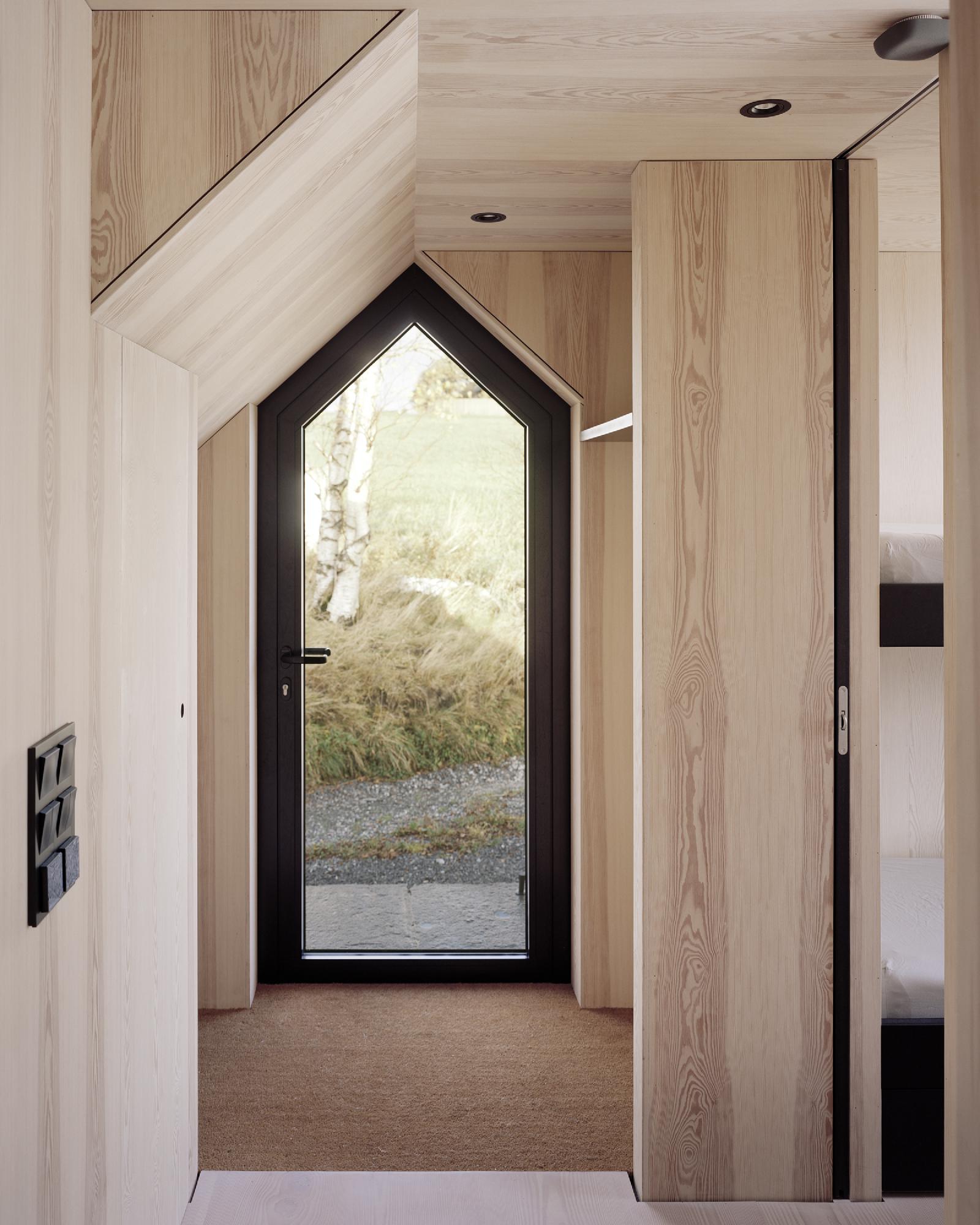 Boat House (Naust) by Espen Surnevik — A gabled entrance portal frames the boathouse threshold, its peaked black-frame door facing the rocky coastal landscape beyond.