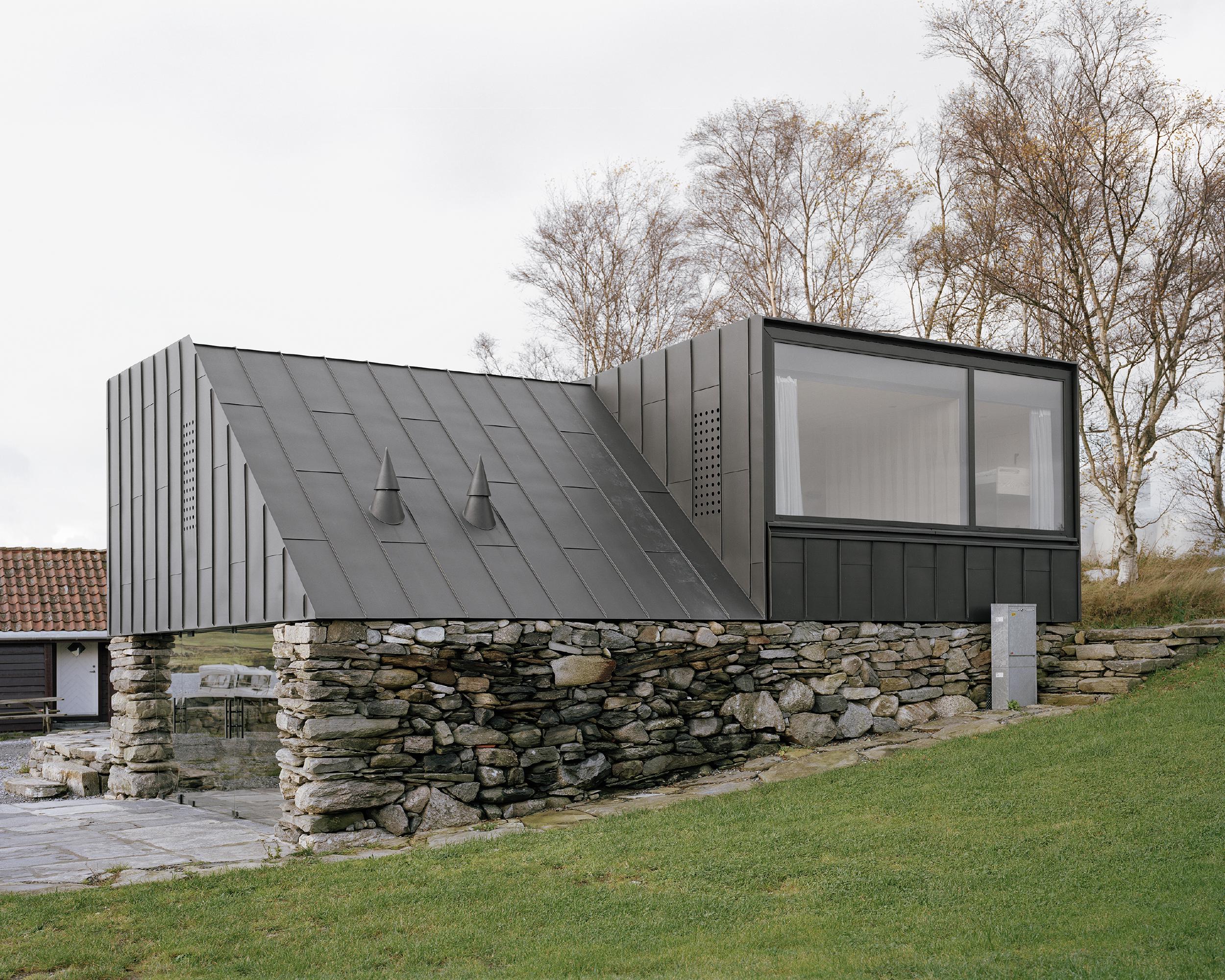 Boat House (Naust) by Espen Surnevik — Espen Surnevik's Naust anchors a minimalist black-clad superstructure to an existing dry-stone foundation wall coursed in irregular grey and ochre blocks.