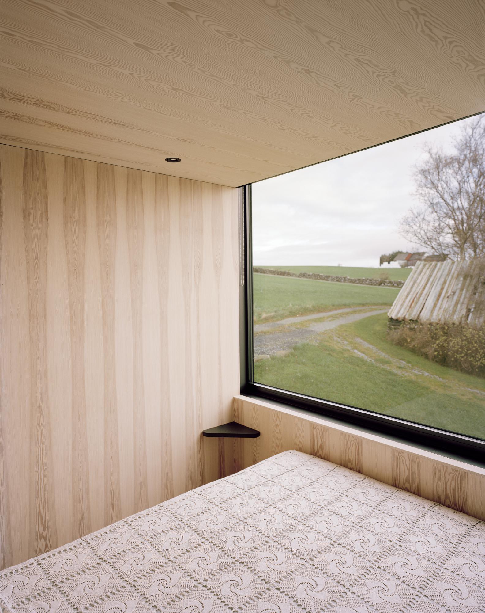 Boat House (Naust) by Espen Surnevik — A minimalist bedroom interior occupies the upper storey of the boathouse, defined by vertical timber cladding in pale ash tones that extends across walls...