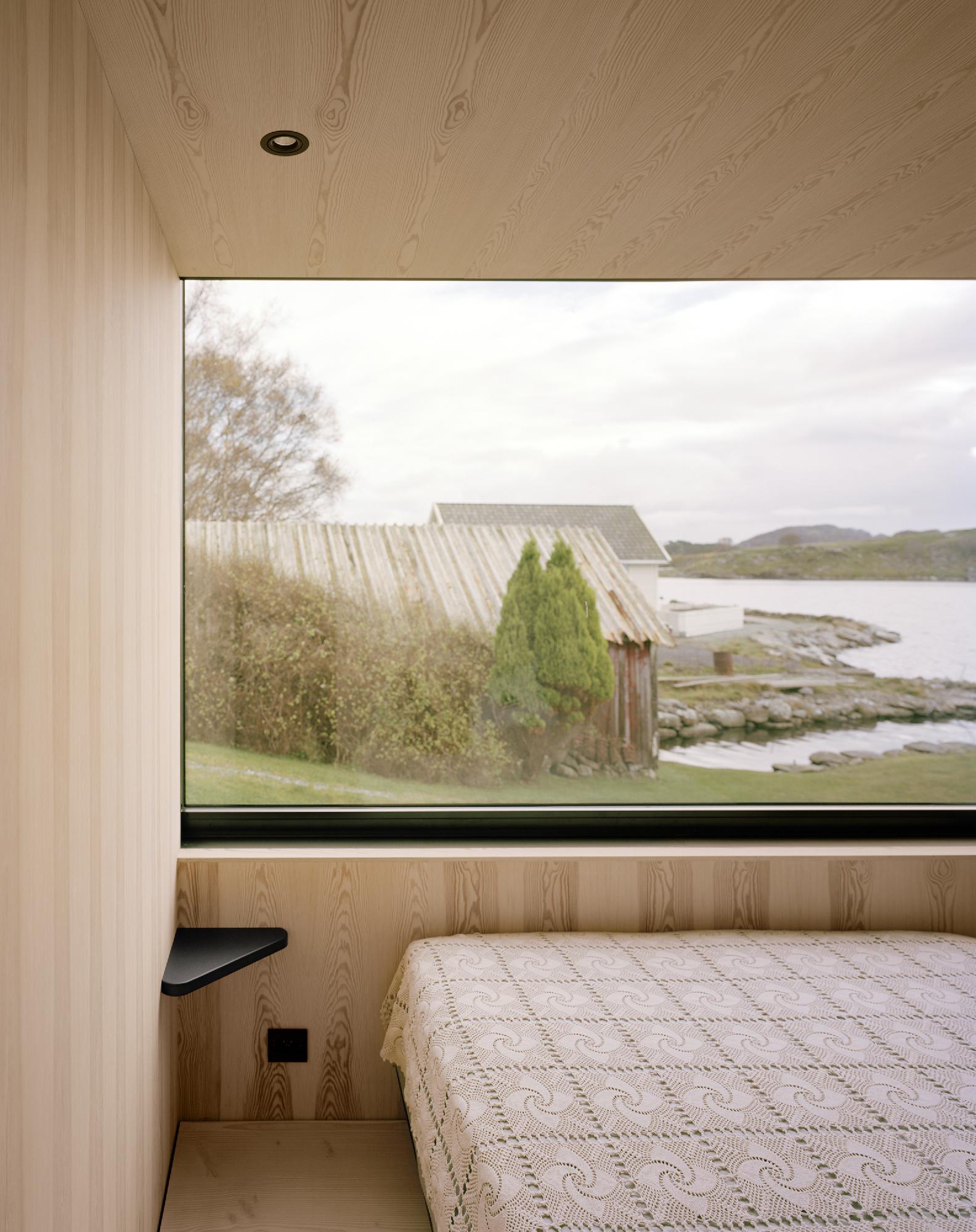 Boat House (Naust) by Espen Surnevik — A bedroom interior framed by a continuous horizontal window band reveals the boathouse's dual material language.