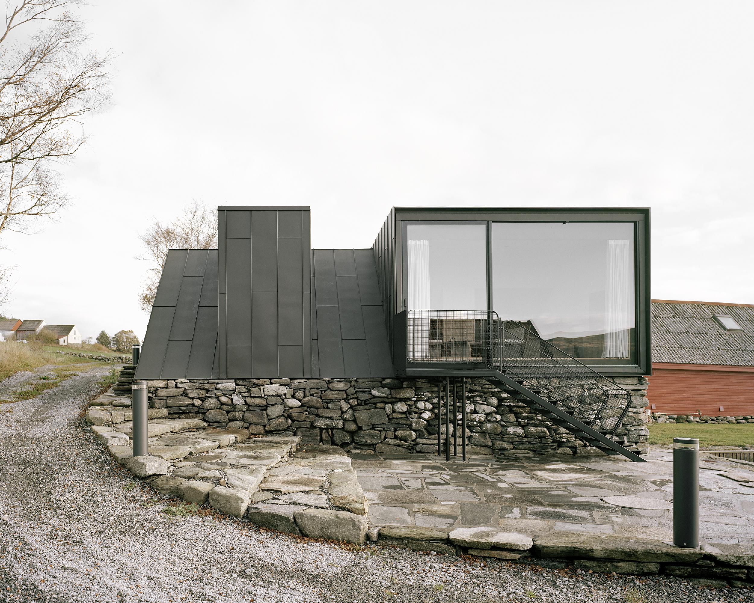 Boat House (Naust) by Espen Surnevik — A contemporary boathouse extension sits elevated on a dry-stone foundation with irregular grey and ochre coursing.