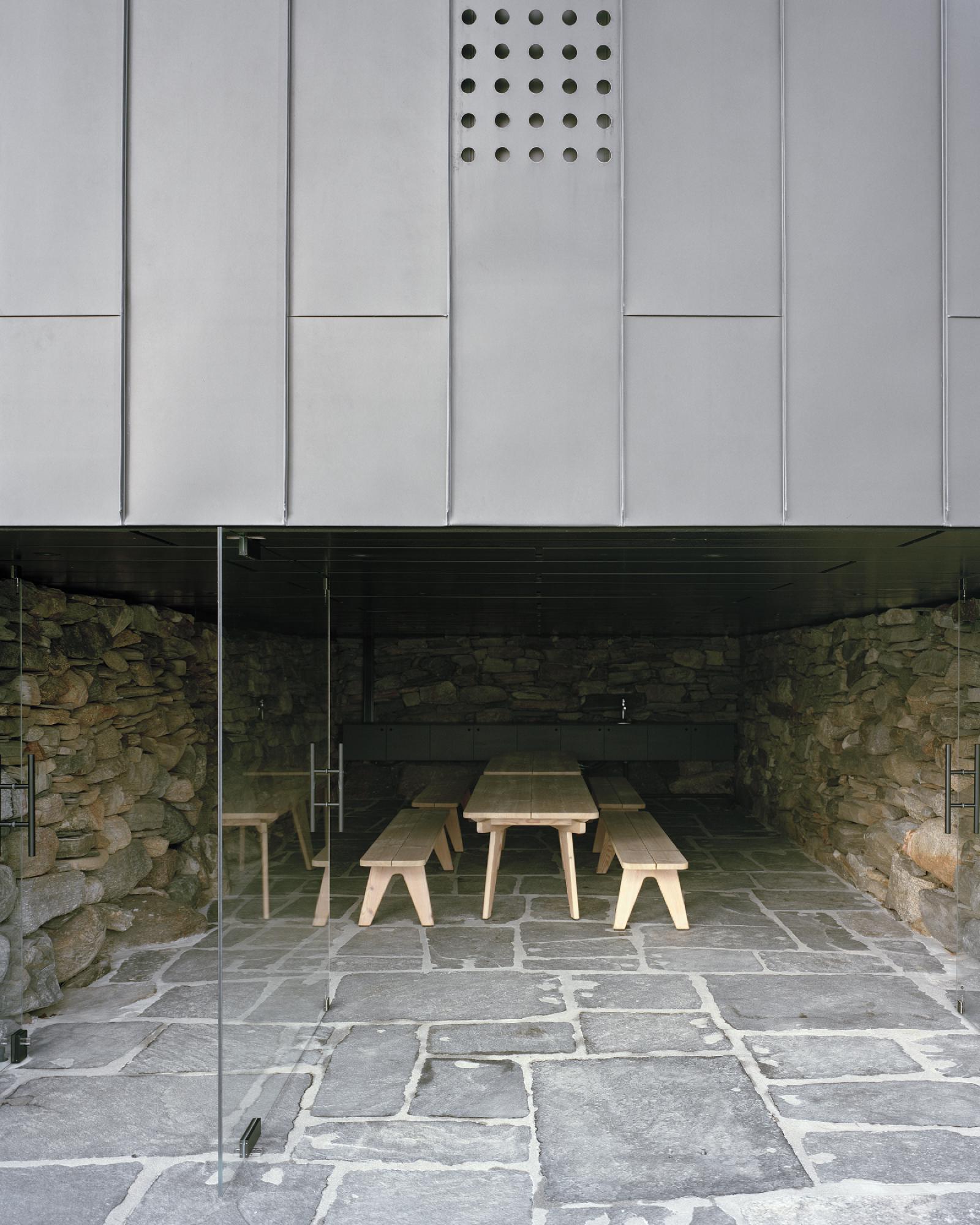Boat House (Naust) by Espen Surnevik — A glazed boathouse pavilion frames a modest timber table and benches set on irregular slate paving.