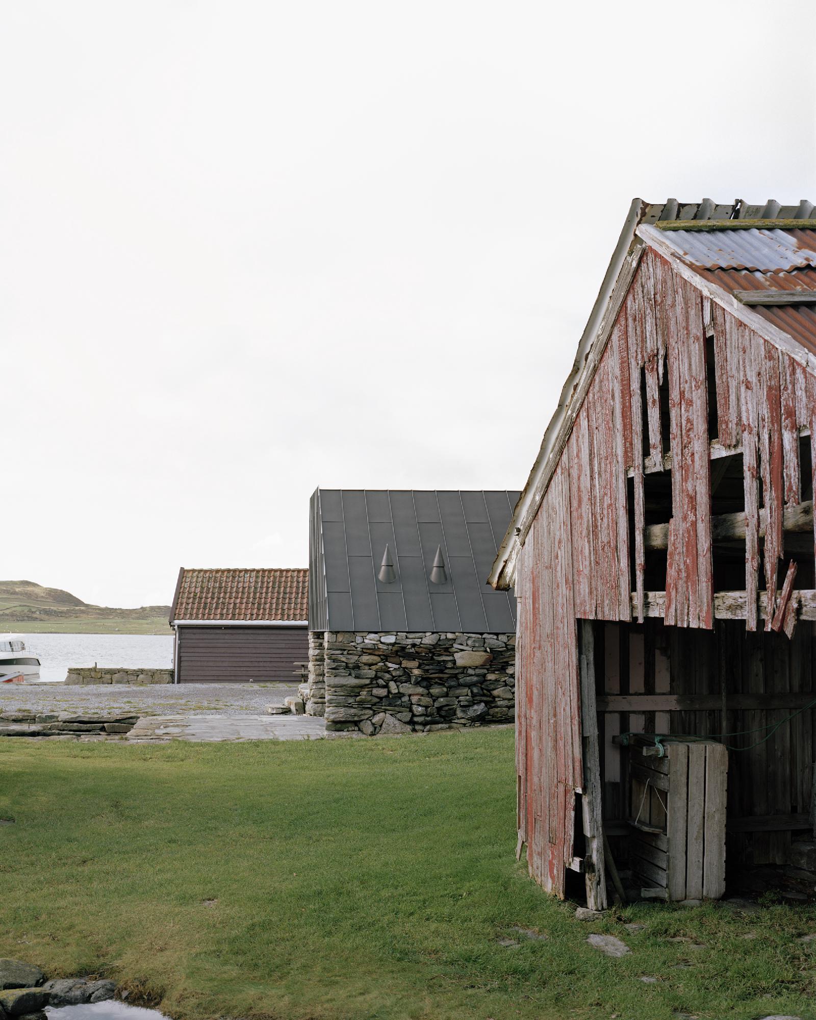 Boat House (Naust) by Espen Surnevik — The boathouse's weathered red timber cladding dominates the foreground, its vertical board siding stripped to bare wood and bleached by coastal exposure.