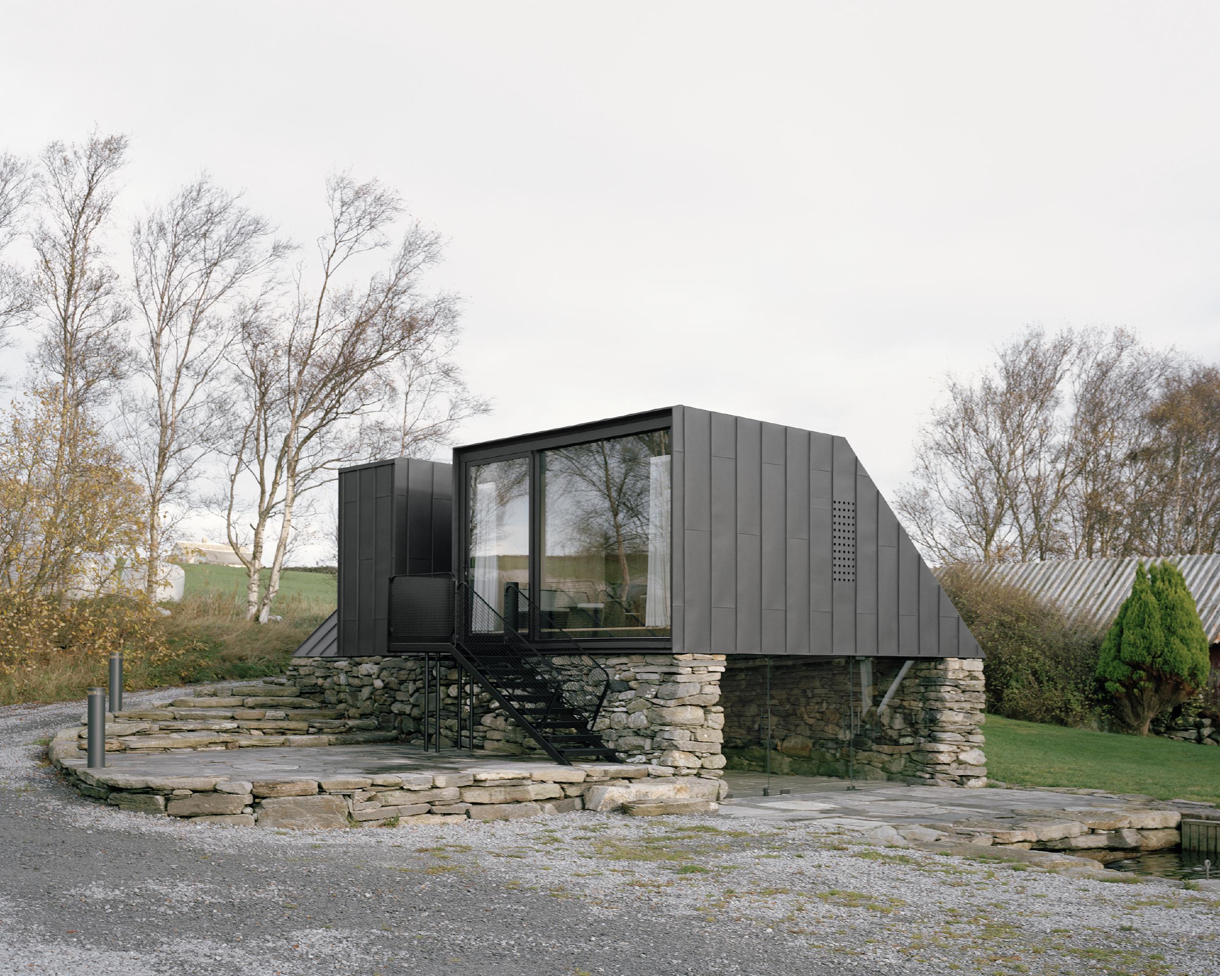 Boat House (Naust) by Espen Surnevik — A modest boathouse rises from a dry-stone foundation of irregular grey and ochre coursing, its weathered masonry anchoring a sharp contemporary intervention.