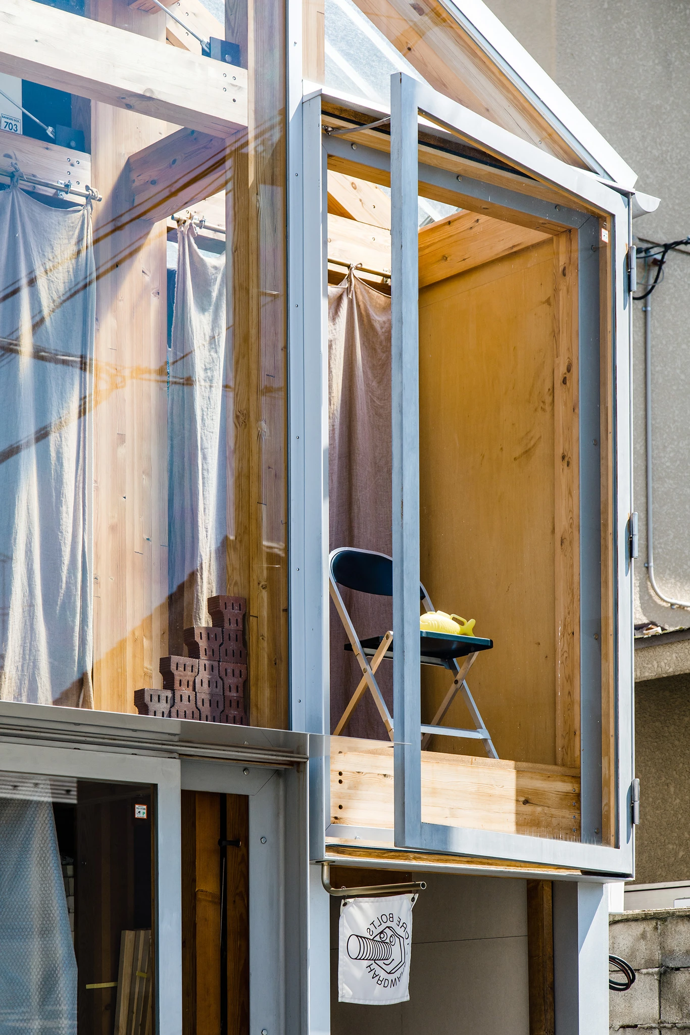 House A/Shop B (Bolts Hardware Store) by KimuraMatsumoto Architects — A narrow vertical storefront in Kyoto's dense urban fabric reveals a timber-framed workshop interior bathed in golden overhead light.