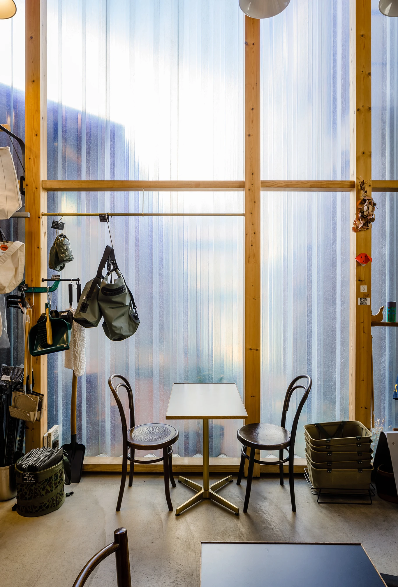 House A/Shop B (Bolts Hardware Store) by KimuraMatsumoto Architects — Interior view of the hardware store's ground-floor workshop, framed by full-height transparent glazing and timber post-and-beam structural frame.