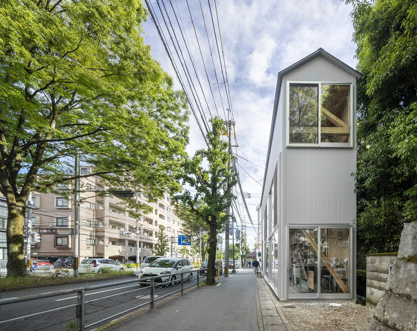 House S/Shop B (ba hütte) by KimuraMatsumoto Architects — A narrow corrugated metal structure with vertical ribbing in cool grey stands perpendicular to a tree-lined Kyoto street.