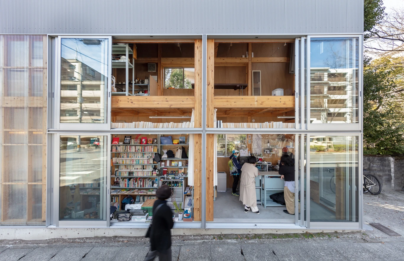 House S/Shop B (ba hütte) by KimuraMatsumoto Architects — A street-facing storefront with full-height glazing reveals a dual-function interior: library shelving stocked with books occupies the lower left section,...