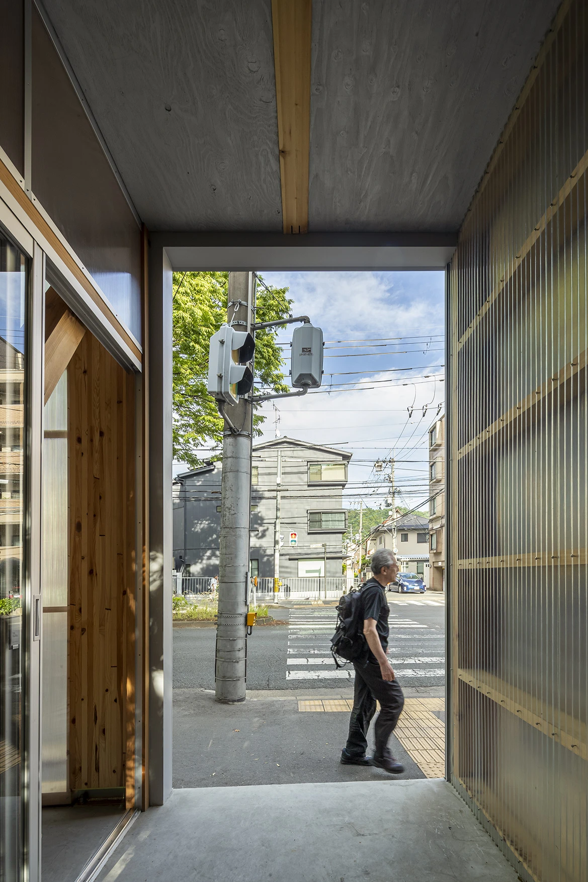 House S/Shop B (ba hütte) by KimuraMatsumoto Architects — View through the recessed threshold of House S/Shop B toward the street, framing a pedestrian crossing beneath a traffic signal mounted on a concrete...