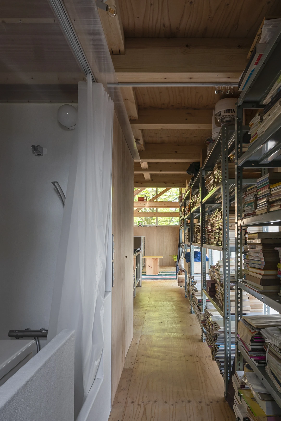 House S/Shop B (ba hütte) by KimuraMatsumoto Architects — Interior corridor of a narrow timber-framed structure lined with industrial metal shelving units densely stacked with compact discs and media.